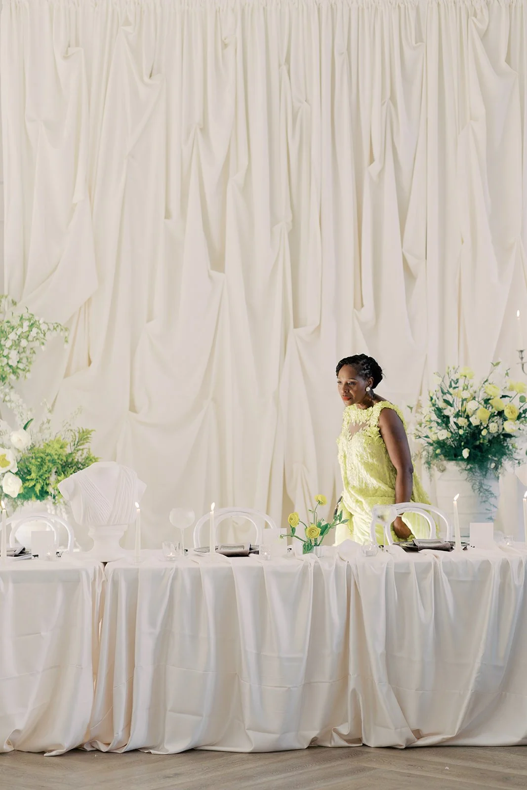 Editorial head table in lemon yellow and white with sculptural floral urns, a classical sculpture, and a draped ivory backdrop at The Bradford