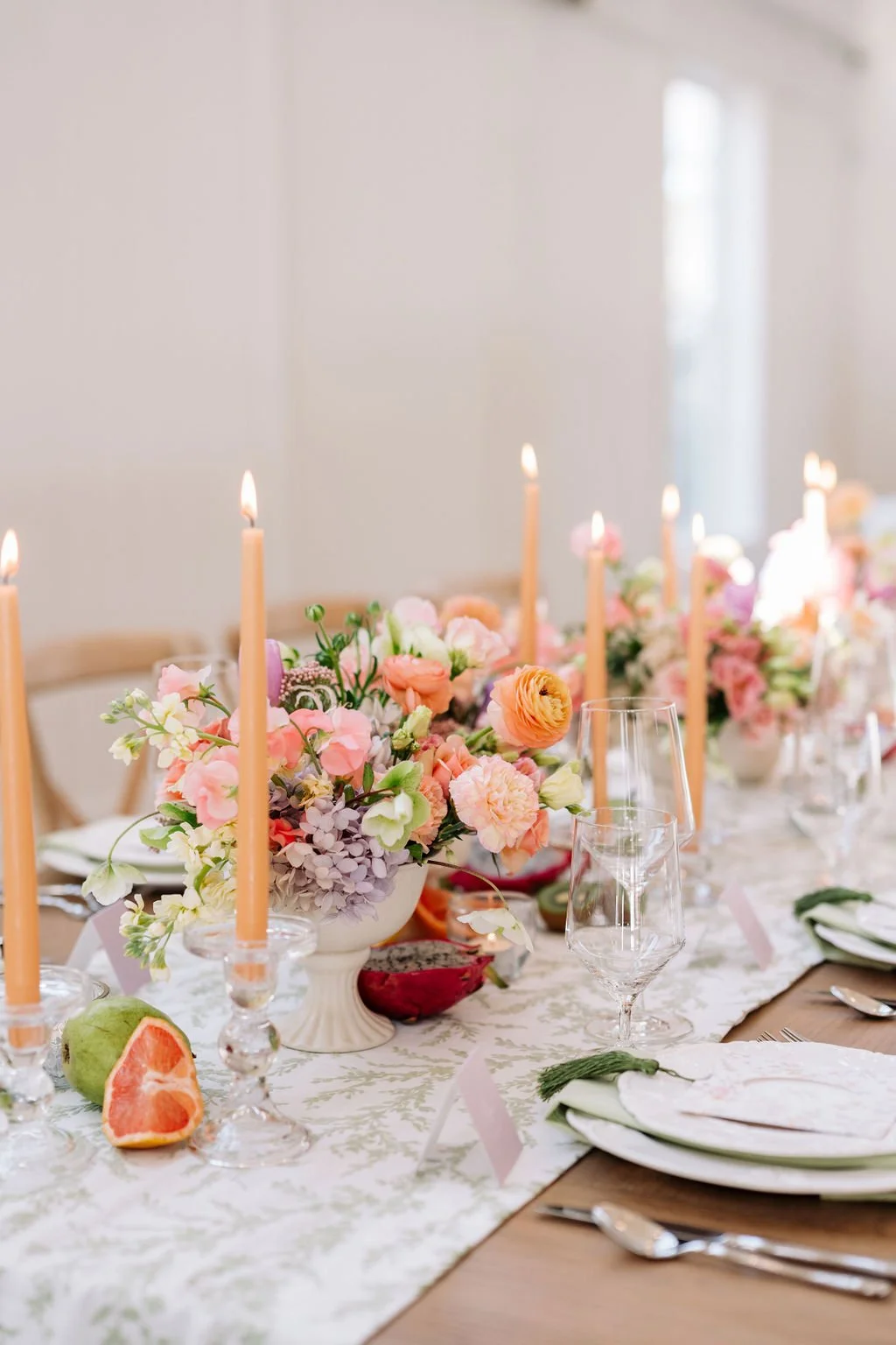 A decorated table with flower arrangements, pink candles, glasses, and plates, set for a celebration or formal event.