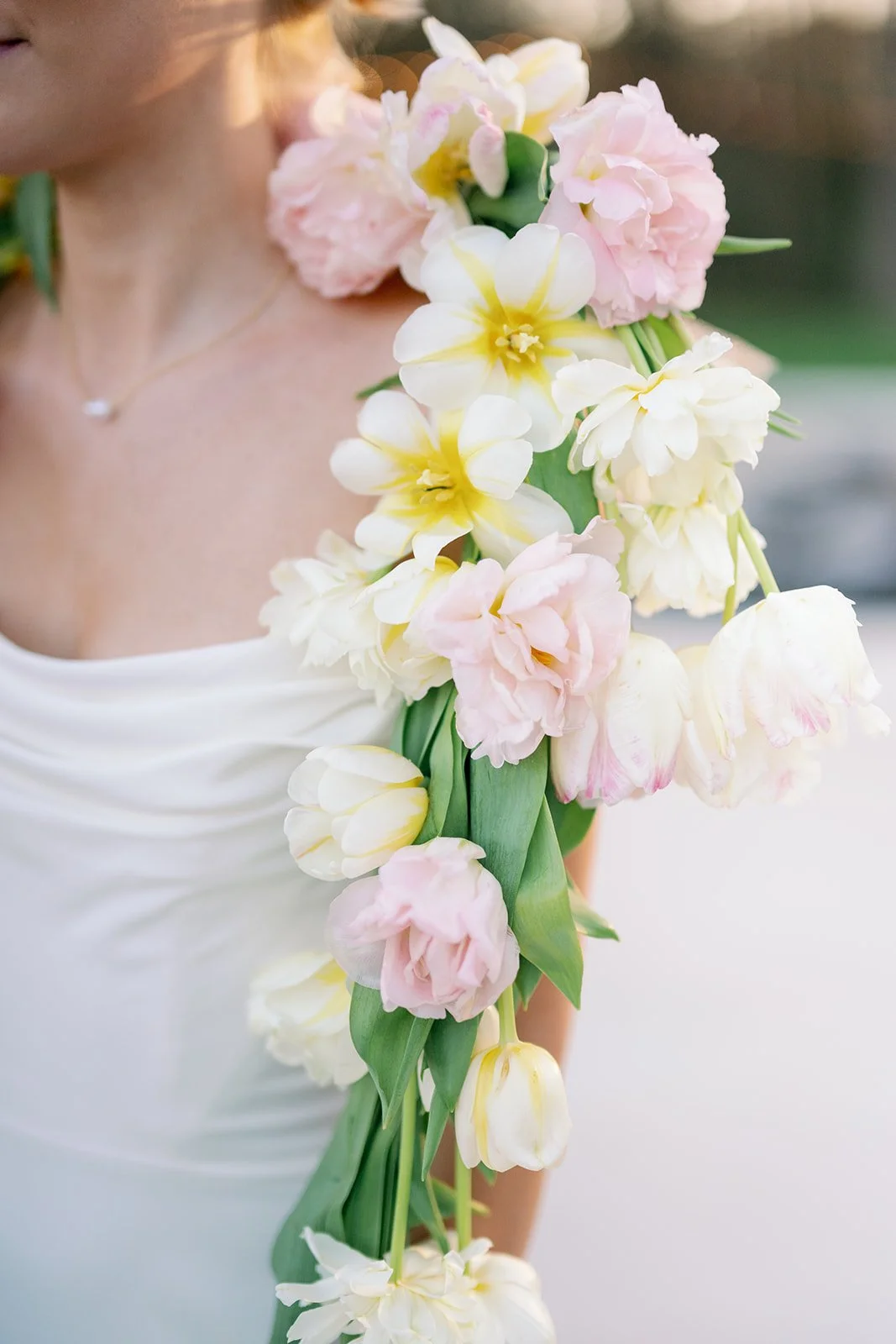 A woman holding a cascading bouquet of pink and white tulips, with part of her white dress visible.
