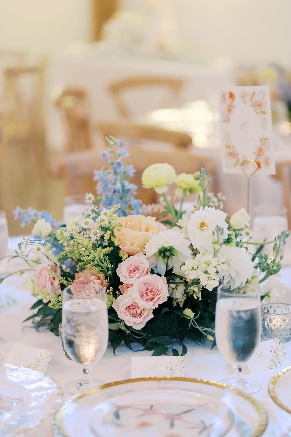 Elegant table setting with a floral centerpiece, water glasses, and gold-rimmed plates at a wedding reception or event.
