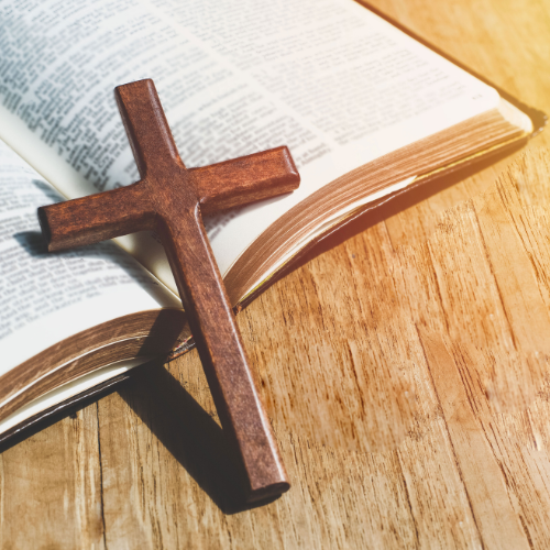 A wooden cross resting on an open Bible on a wooden surface.