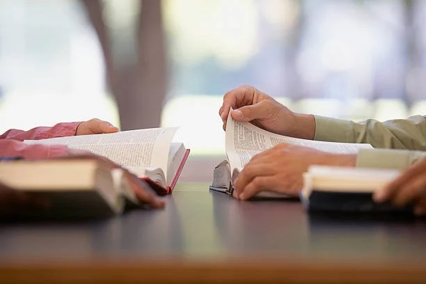 People studying with open books on a table outside in a park.