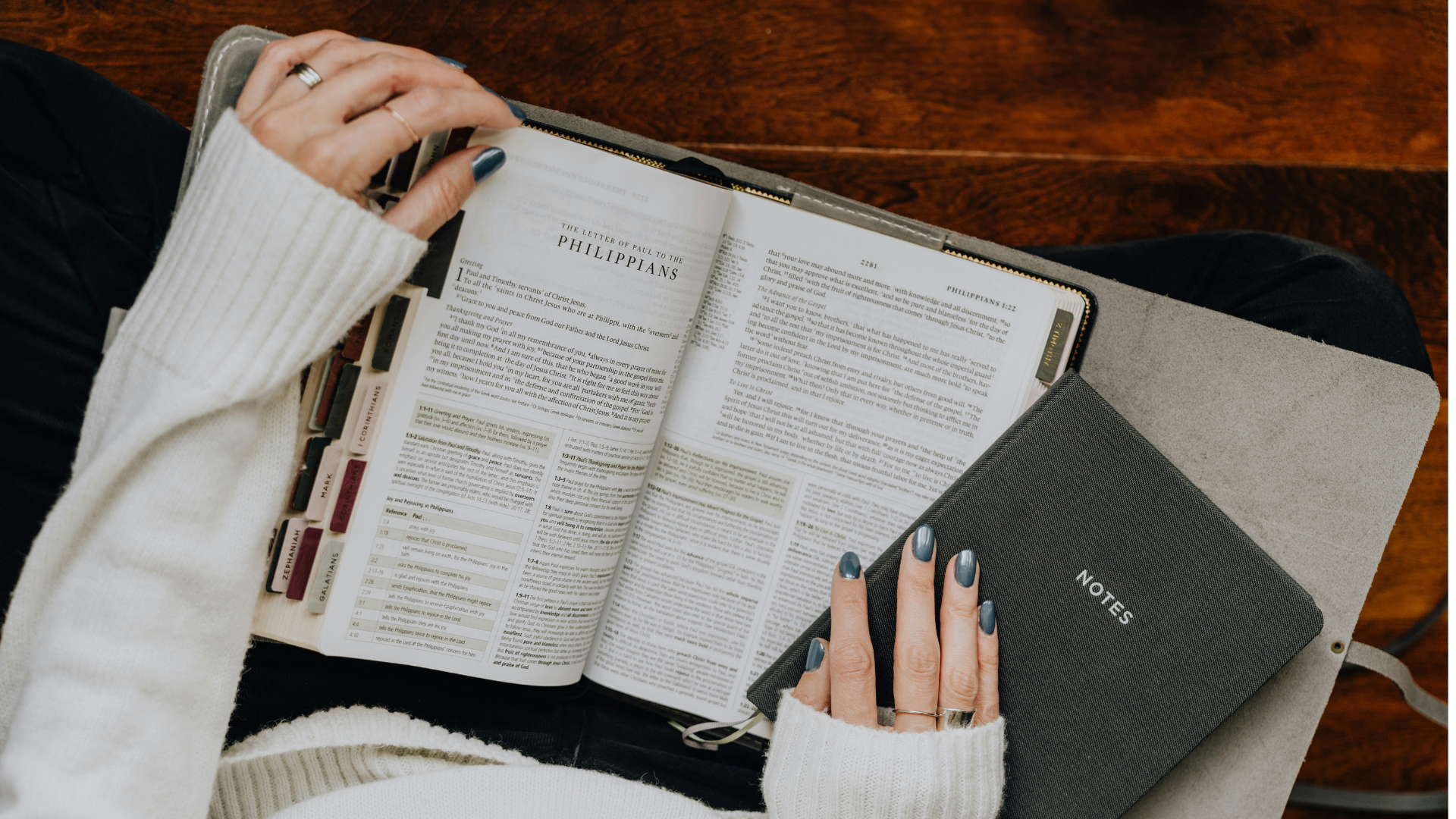 Person reading a Bible with tabs, holding a notebook labeled 'Notes'