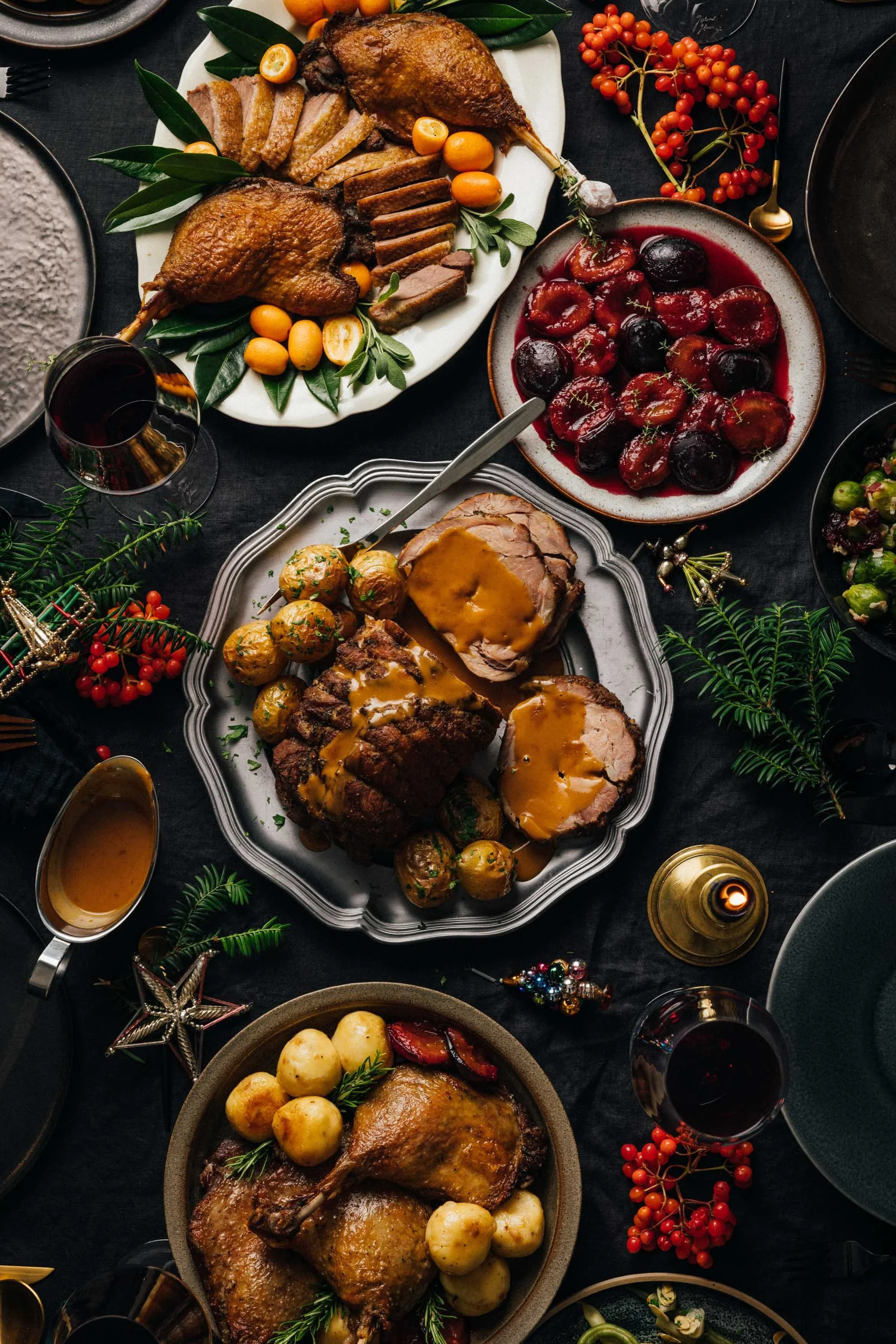 Festlich gedeckter Tisch mit Weihnachtsessen, darunter Braten mit Sauce, Rotkohl, Gänsekeulen mit Salzkartoffeln, Roastbeef und verschiedene Beilagen, sowie Weihnachtsdeko und Gläser mit Rotwein.