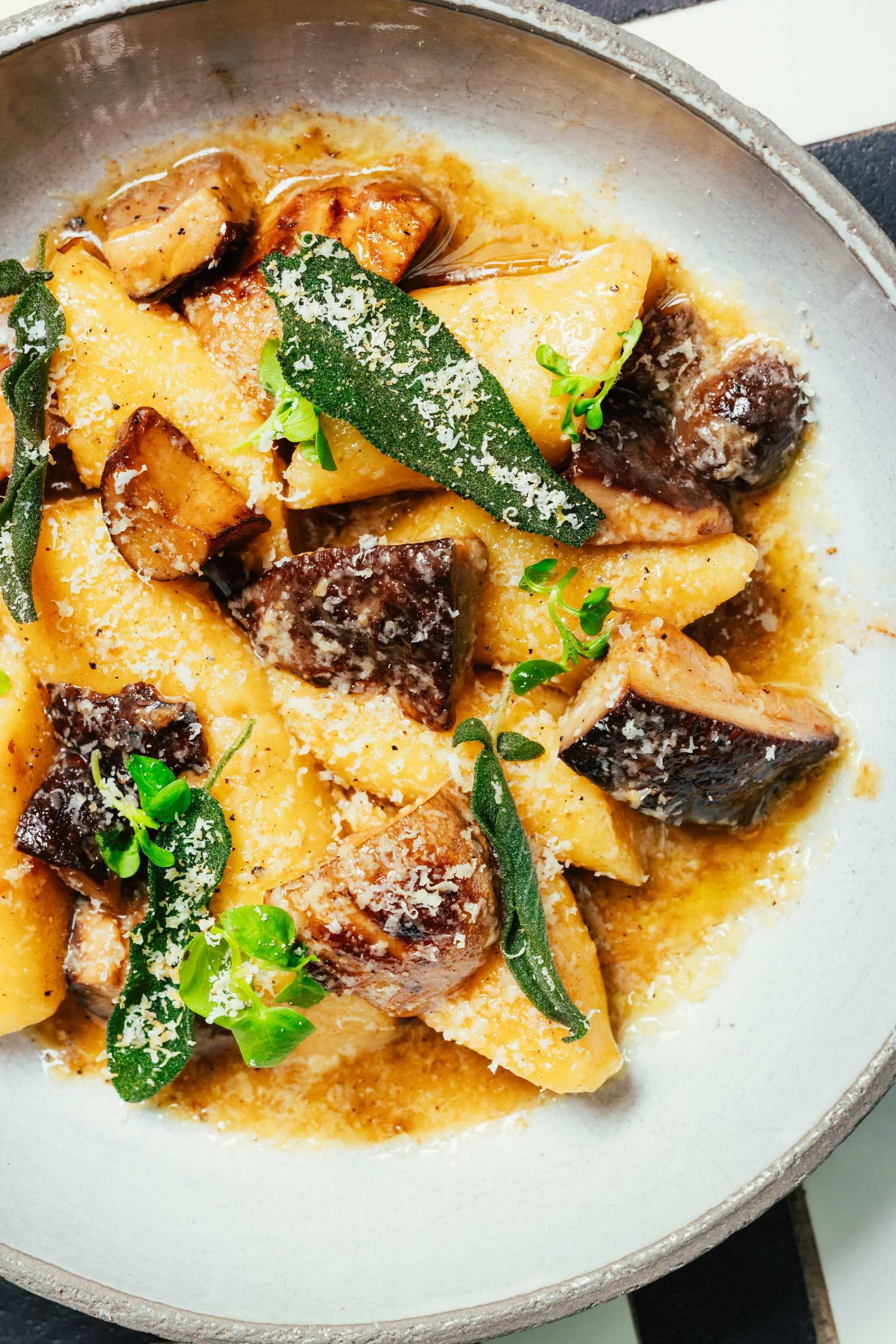 Italienisches Gericht mit Ravioli, braunen Pilzen, Salbeiblättern und Parmesan in einer cremigen Sauce