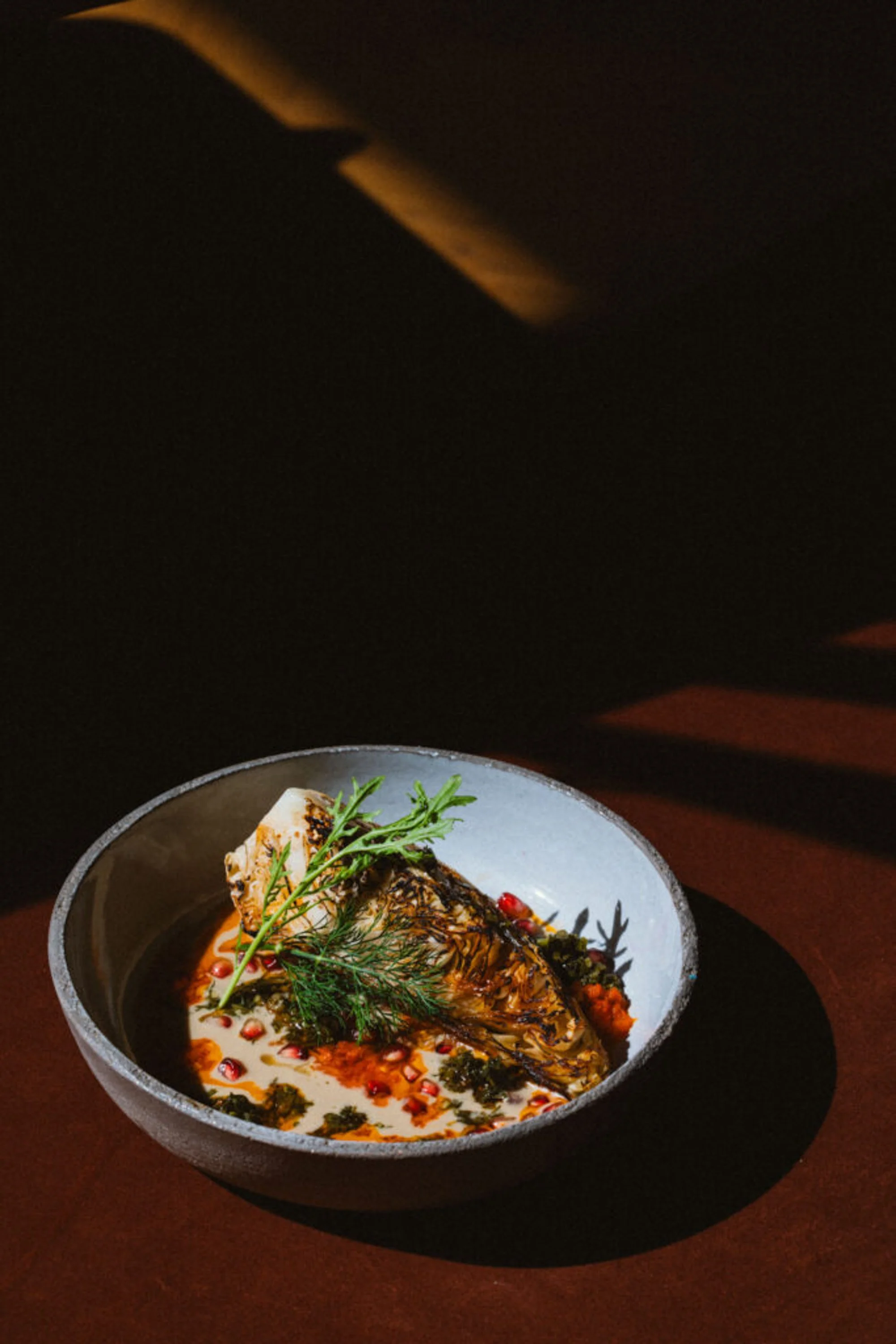 Ein Teller mit gegrilltem Fisch, garniert mit Kräutern, in einer cremigen Sosse mit roten Beeren, auf dunklem Hintergrund.