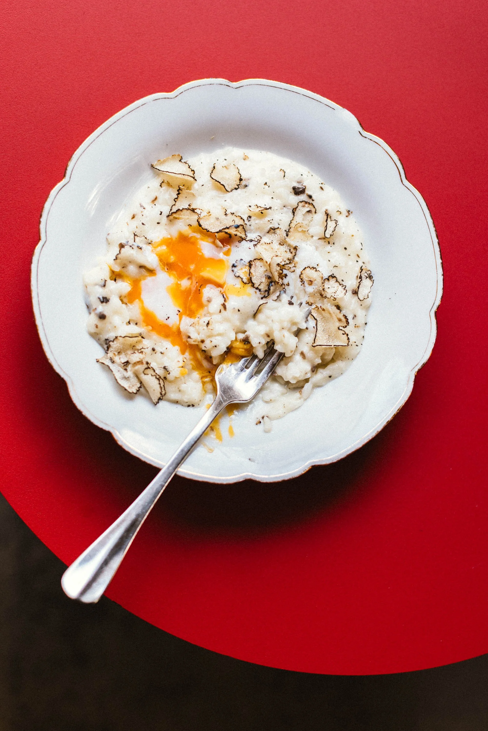 Ein Teller mit Rührei, schwarzen Trüffelscheiben und einem Löffel, auf einem rot-schwarzen Hintergrund.