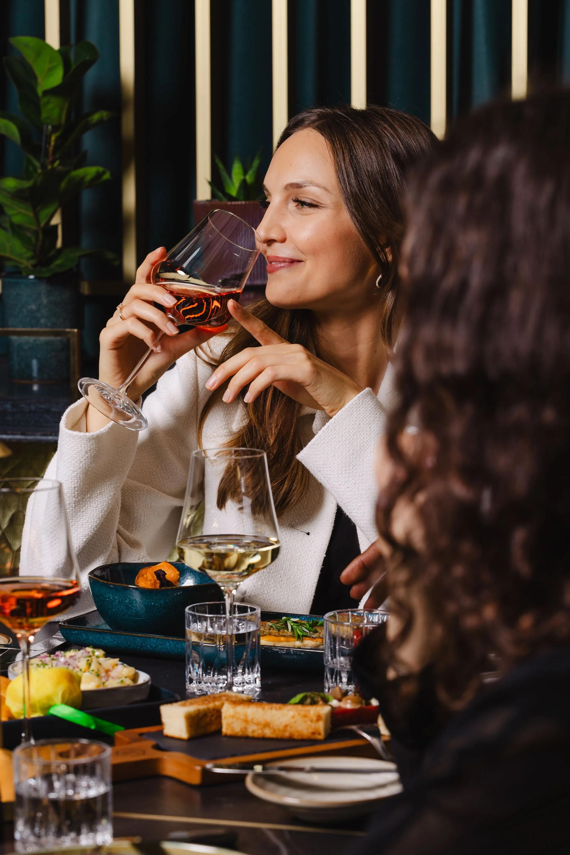 Eine Frau, die ein Glas Rotwein in einem Restaurant hält, während andere Personen mit Getränken und Speisen am Tisch sind.