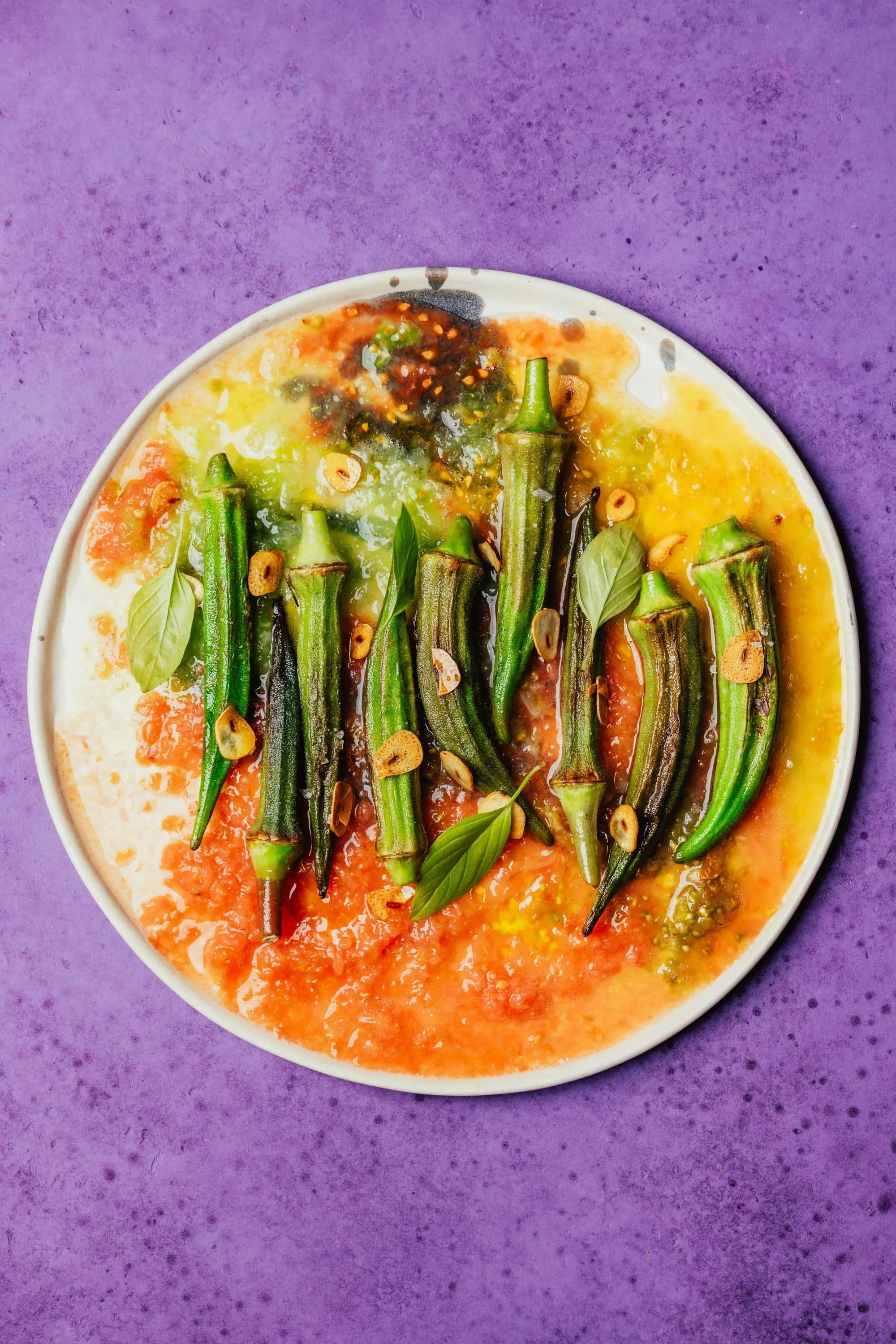 Gedünstete okra mit Knoblauch, Basilikum und Chili in einer weißen Schüssel auf lila Hintergrund.