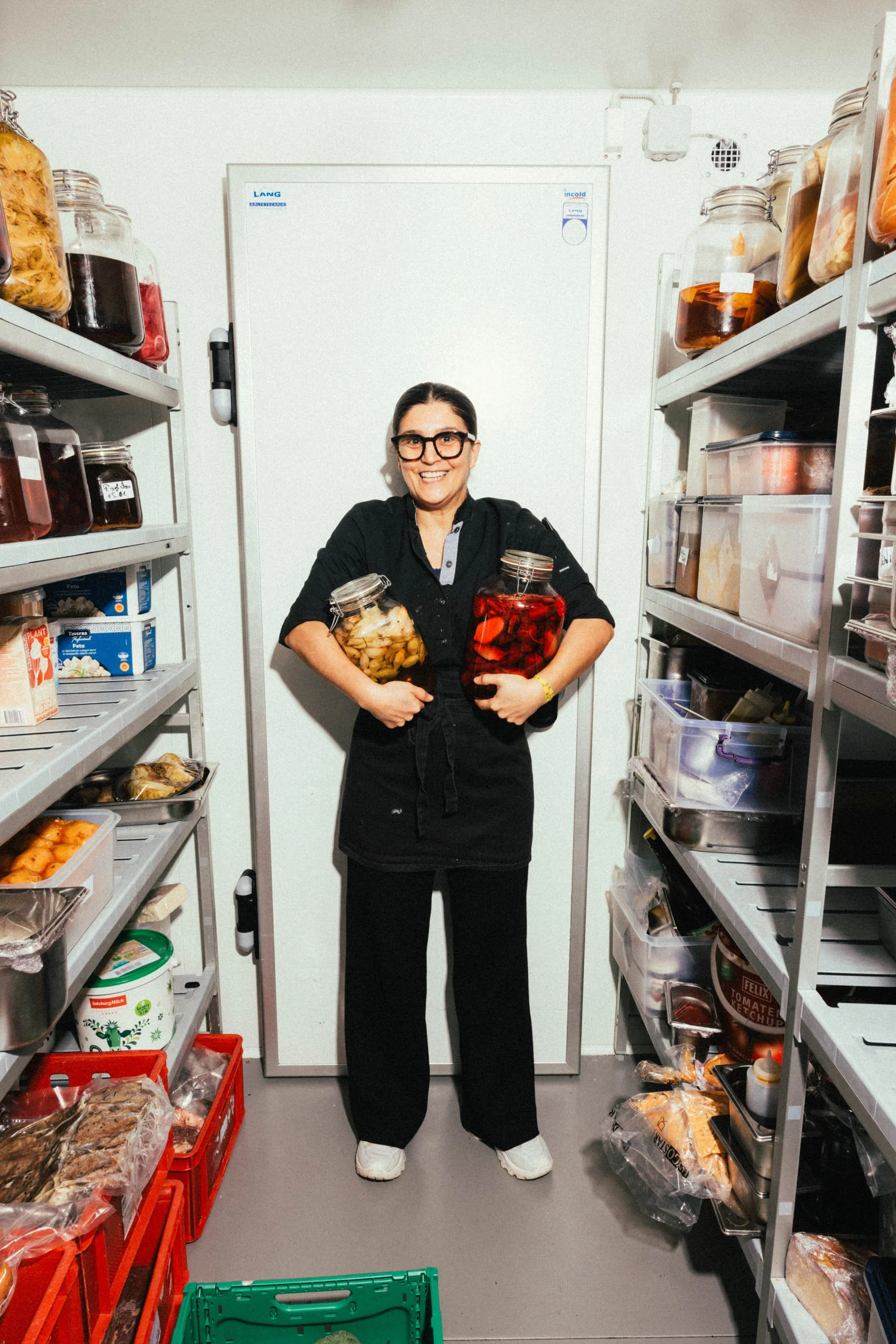 Frau in einem Lebensmittellager, die zwei Einmachgläser mit eingelegtem Gemüse hält.