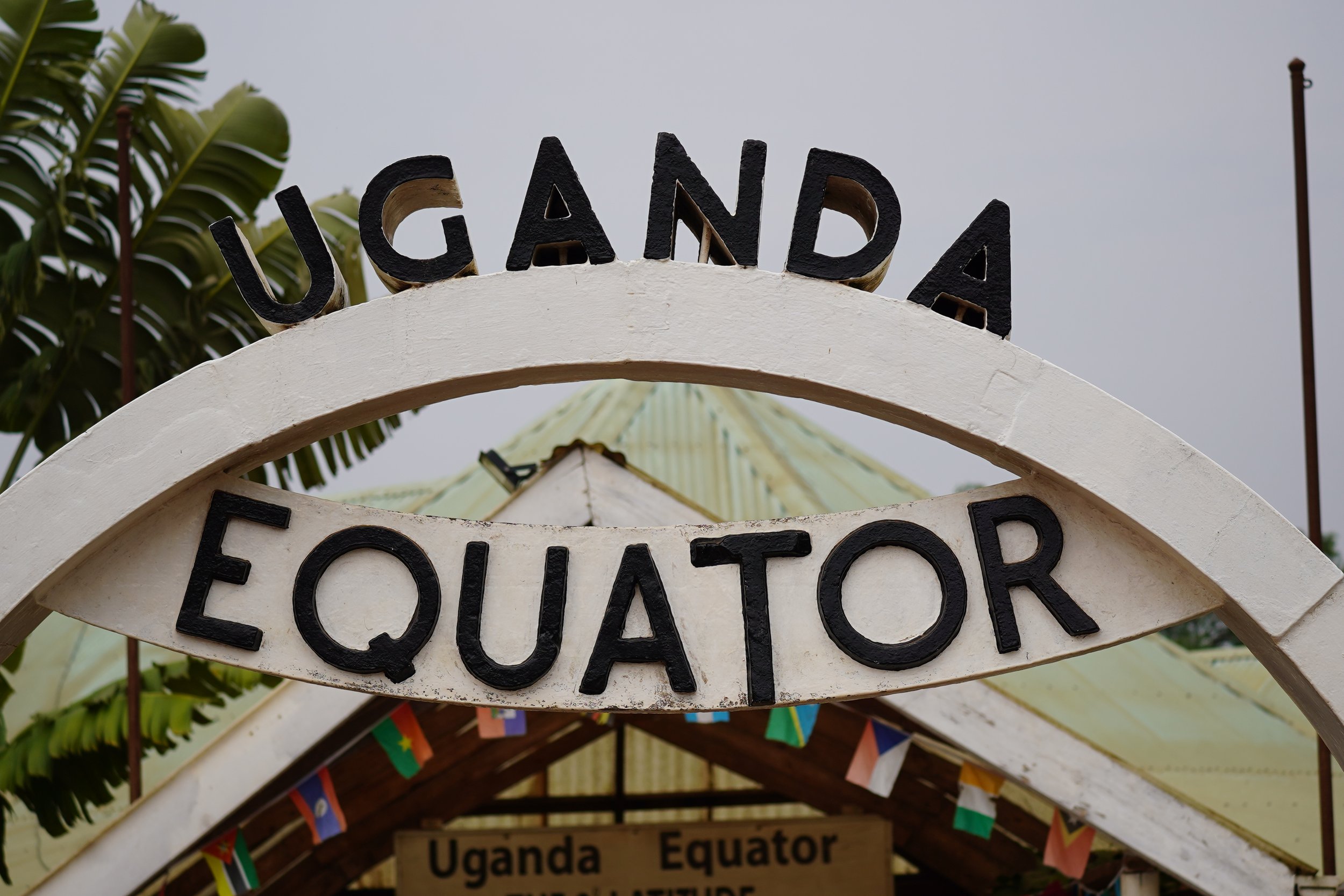 Sign reading 'UGANDA' and 'EQUATOR' at the equator crossing point with flags hanging underneath.