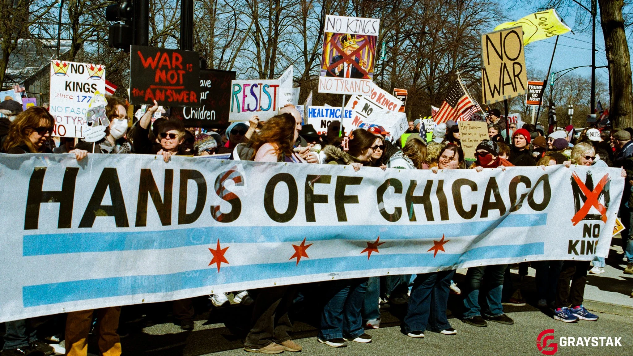 A large group of people participating in a protest or march, holding signs and banners advocating against war and for peace. The main banner reads 'HANDS OFF CHICAGO', with many other smaller signs behind it protesting against kings, war, and tyrants