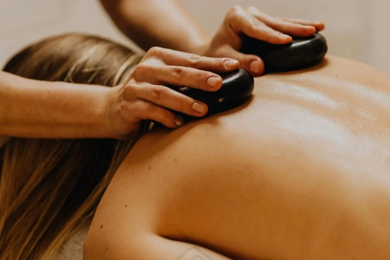 Person receiving a hot stone massage on their back, with stones placed on the skin and hands gently massaging.