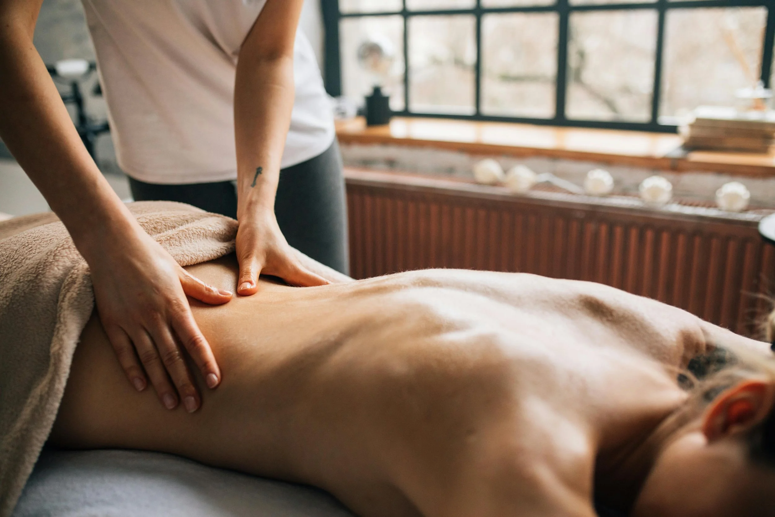 A person receiving a massage on their back in a wellness spa or massage therapy setting, with a therapist using their hands to apply pressure.