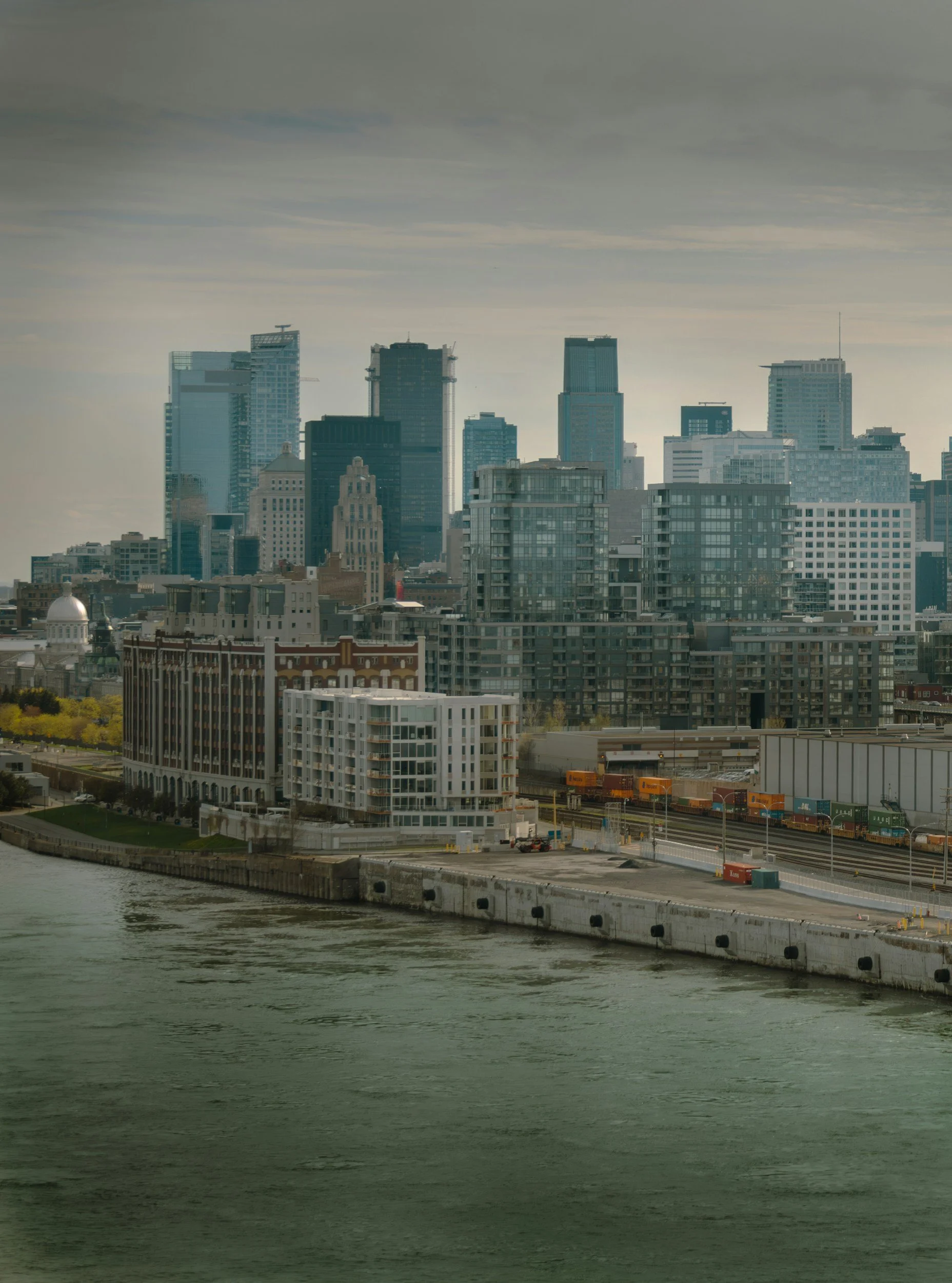 City skyline with tall skyscrapers, a river in the foreground, and a train passing by.