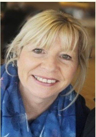 Close-up of a smiling woman with blonde hair, wearing a blue scarf.