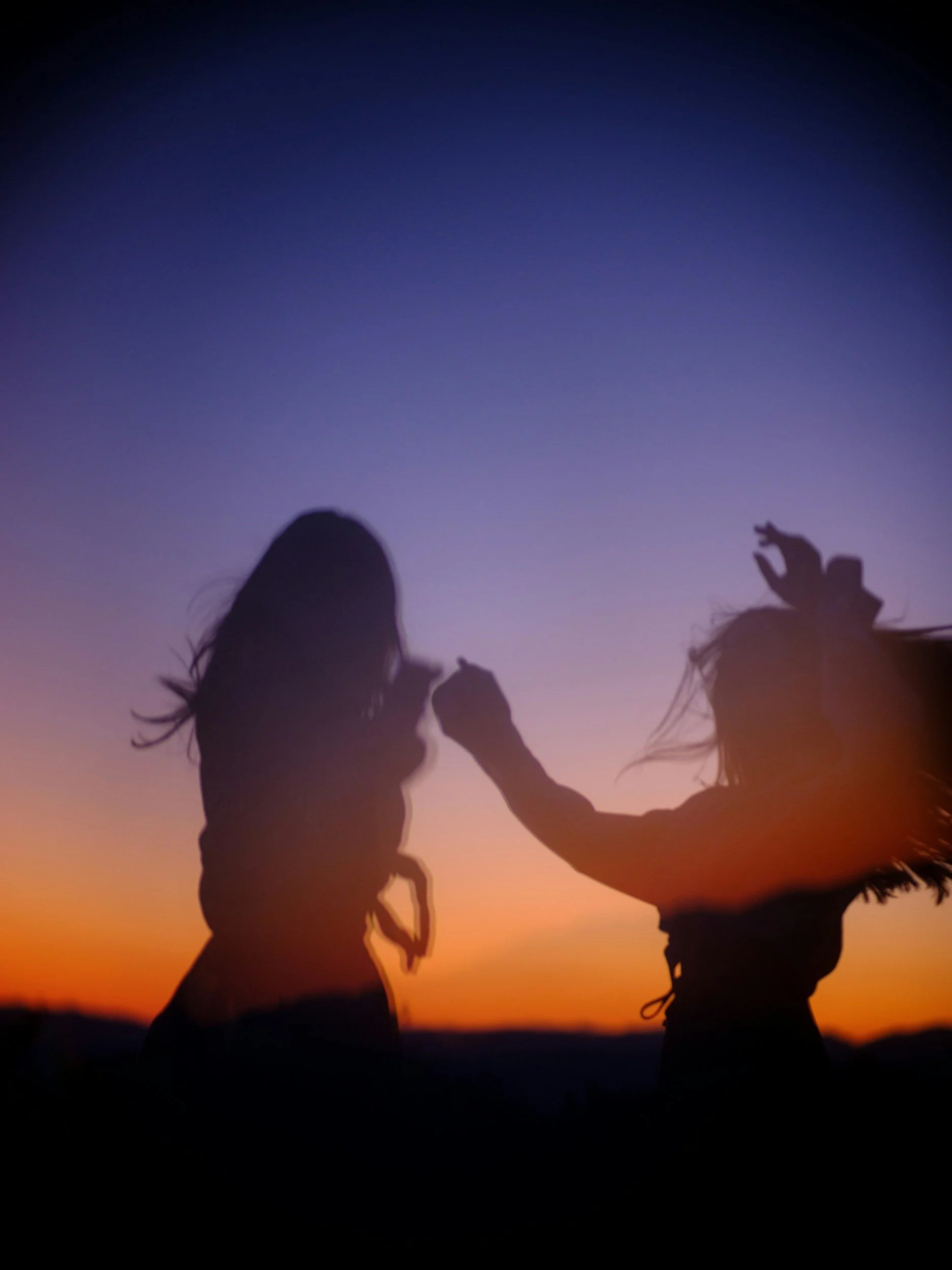 Silhouettes of two girls holding hands during sunset with a colorful gradient sky in the background.