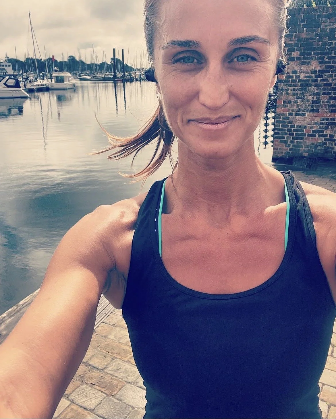 A close up photo of a woman near a marina with boats and sailboats in the background.