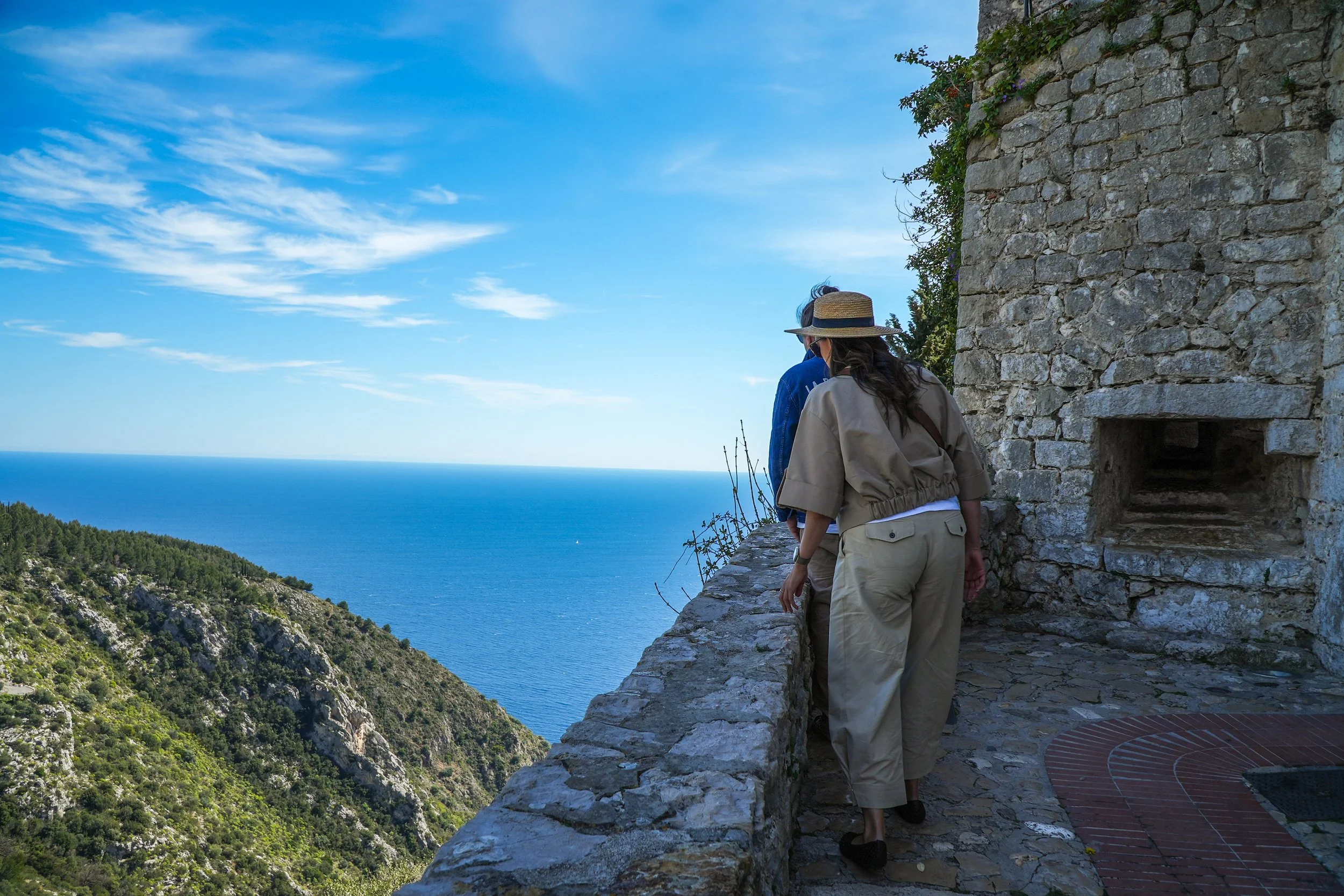 Deux personnes regardant la vue sur la mer depuis un site historique avec un mur en pierre.