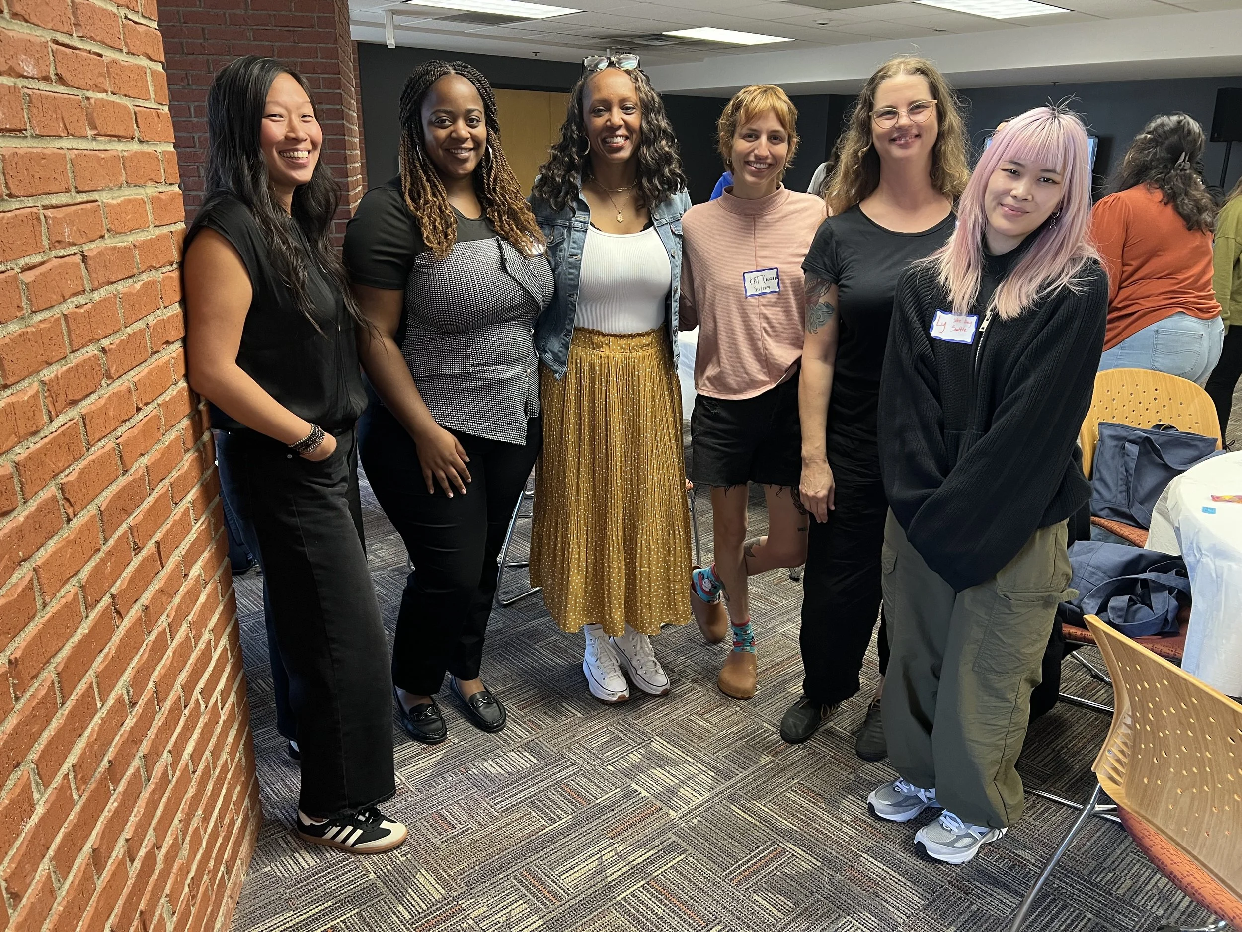 Six women standing together at an indoor event, smiling for the photo.