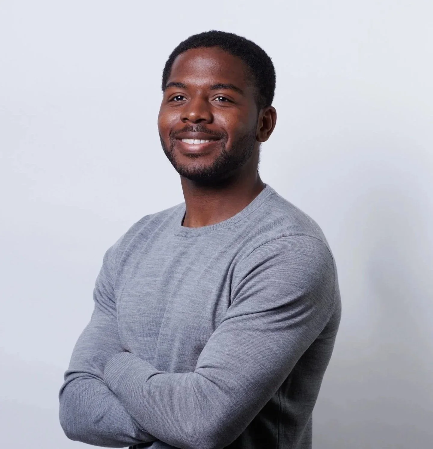Devon Horace, angel investor and Business Strategist, smiling, arms crossed, wearing a gray long-sleeve shirt, standing against a plain white background.