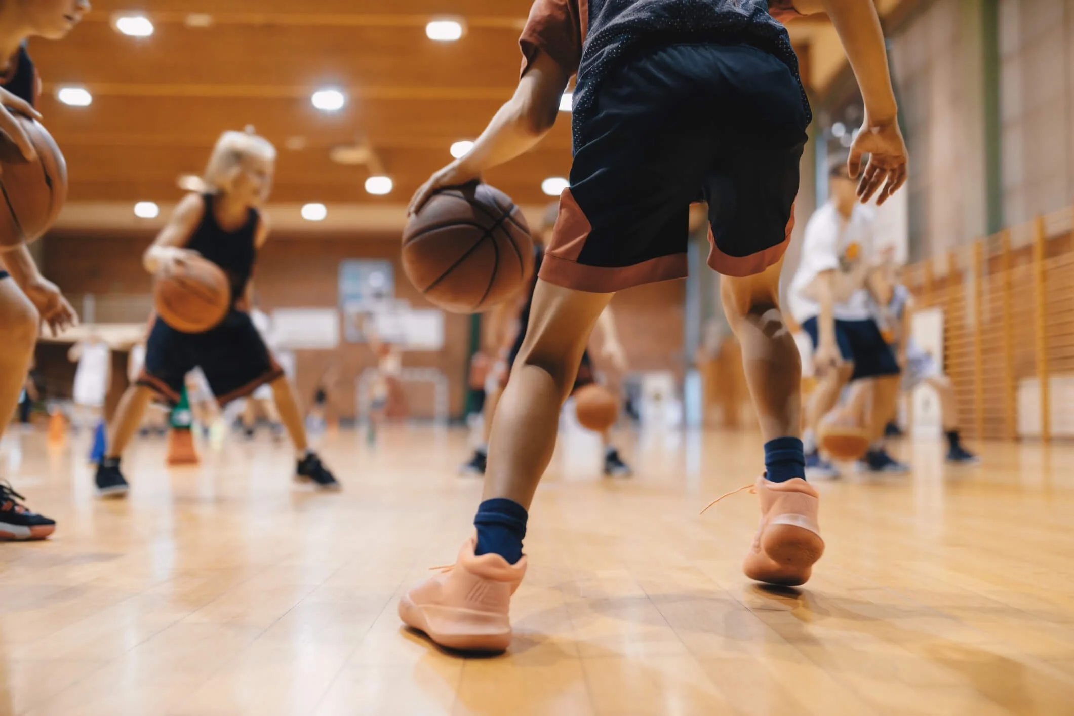 Children participating in a basketball practice in an indoor gym, dribbling basketballs.