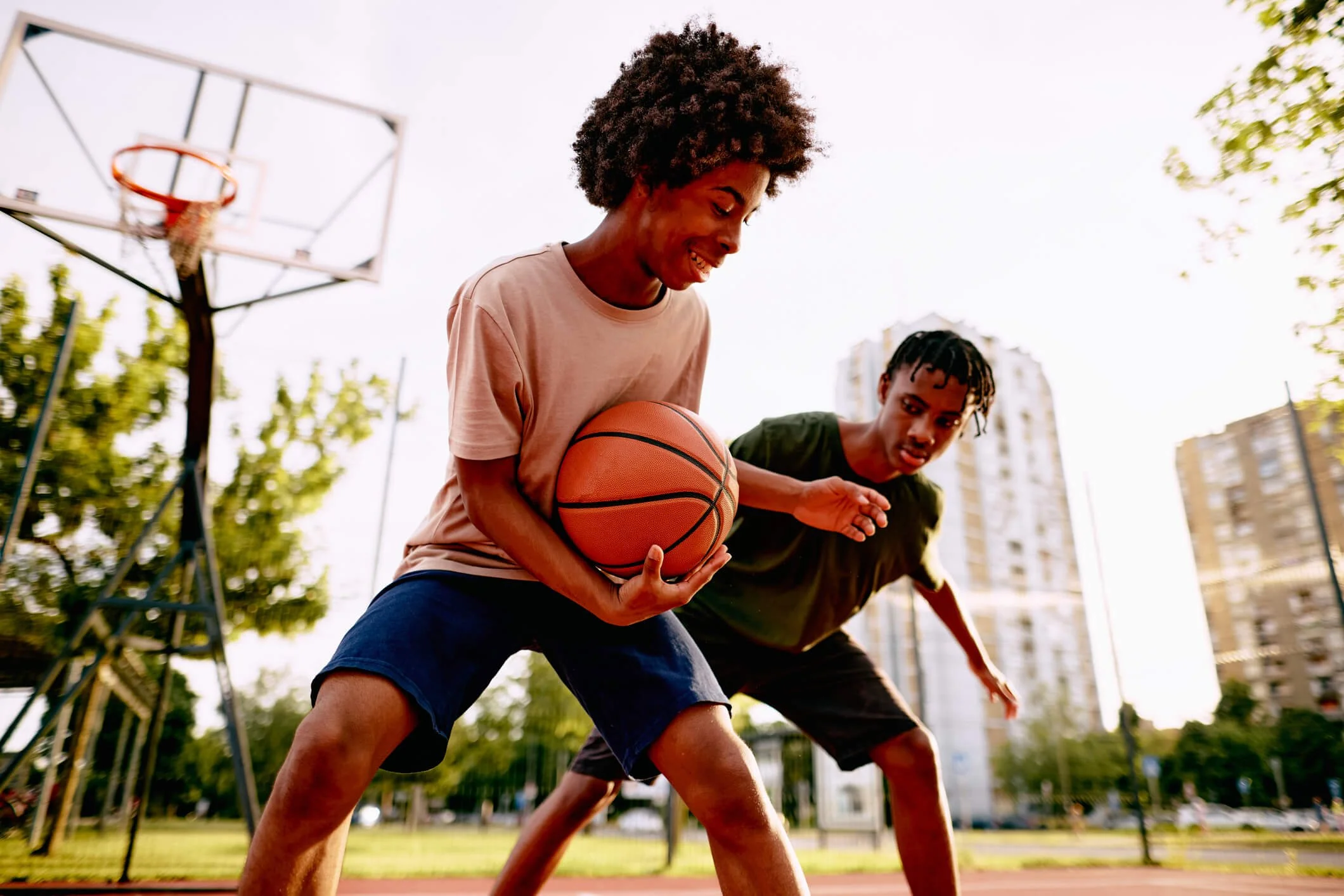 Two young men playing basketball on an outdoor court.