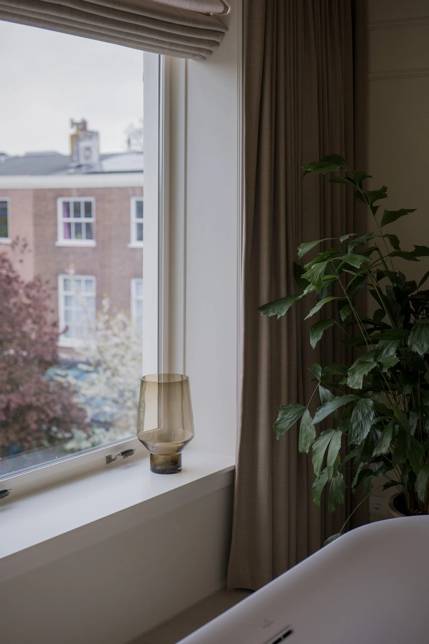 Interieur van een kamer met een venster, een gouden vaas op de vensterbank, een groene kamerplant en beige gordijnen.