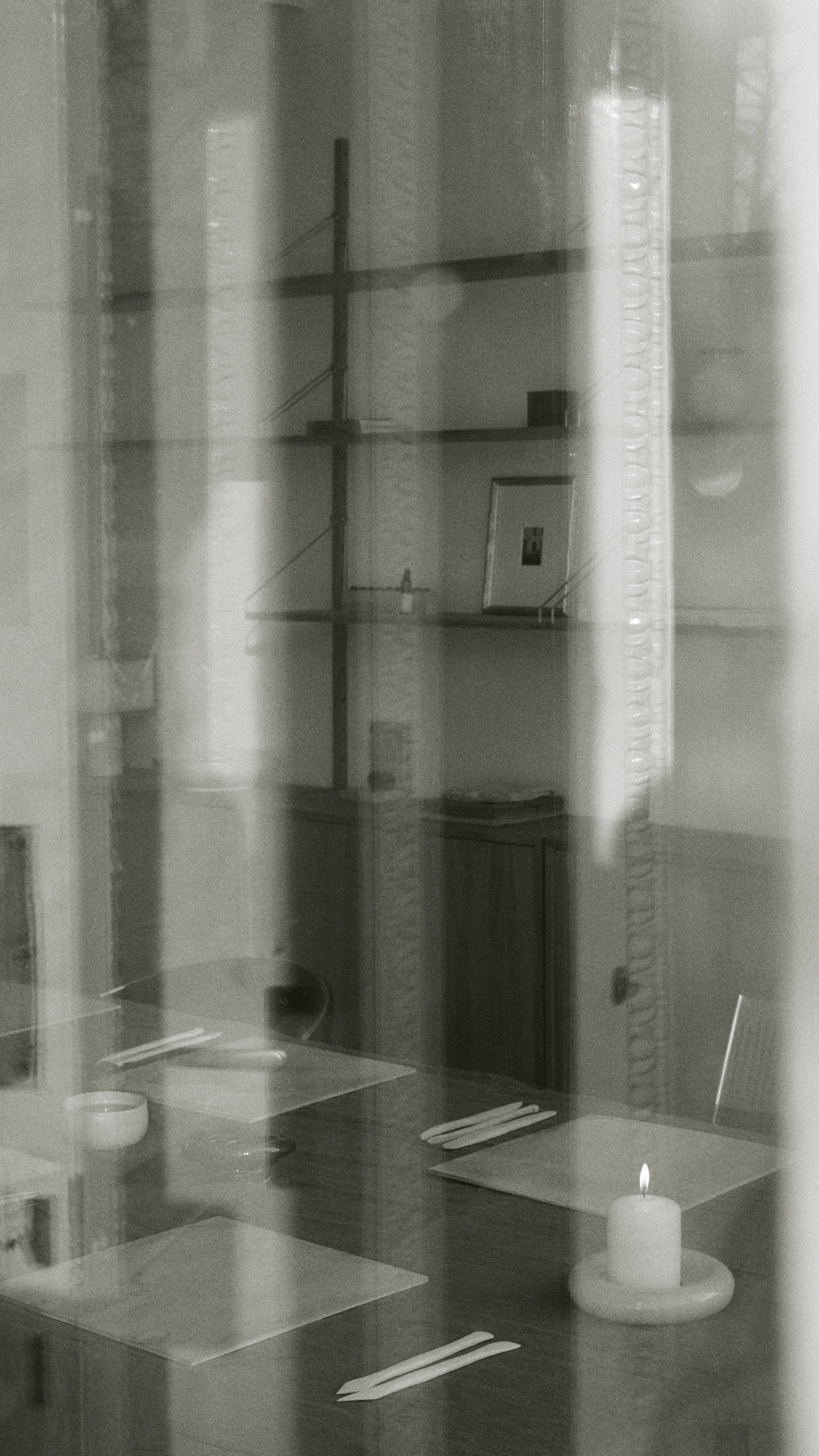 Een gesloten restaurant tafel met bestek, een waxinelichtje en een servet, gezien door een raam metday reflecties.