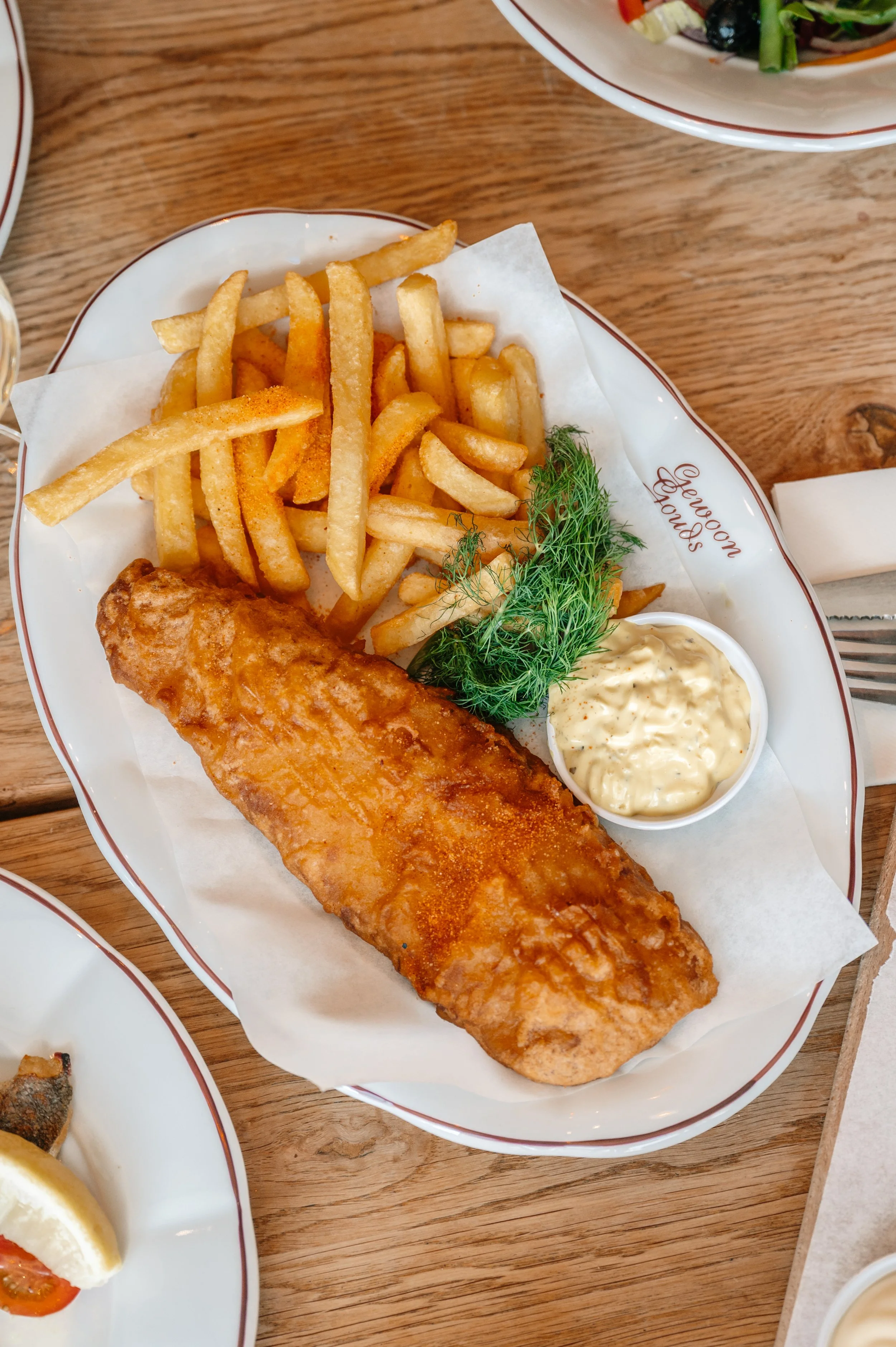 Fried fish served with French fries, tartar sauce, and fresh dill on a white plate with 'Leroux Foods' written on it.