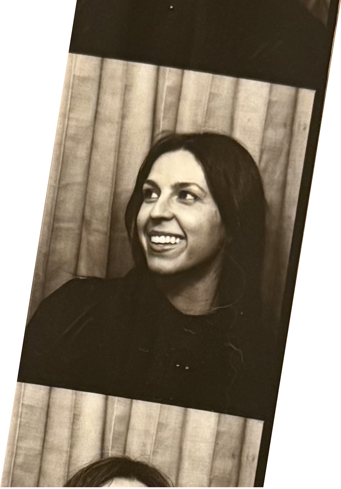 Black-and-white portrait of a woman smiling, with dark hair, in front of a wooden background.