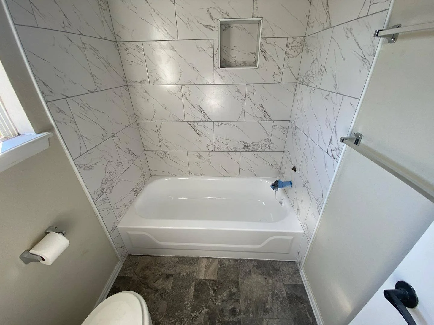 Bathroom with marble-tiled walls, a bathtub, a window, and a towel bar.