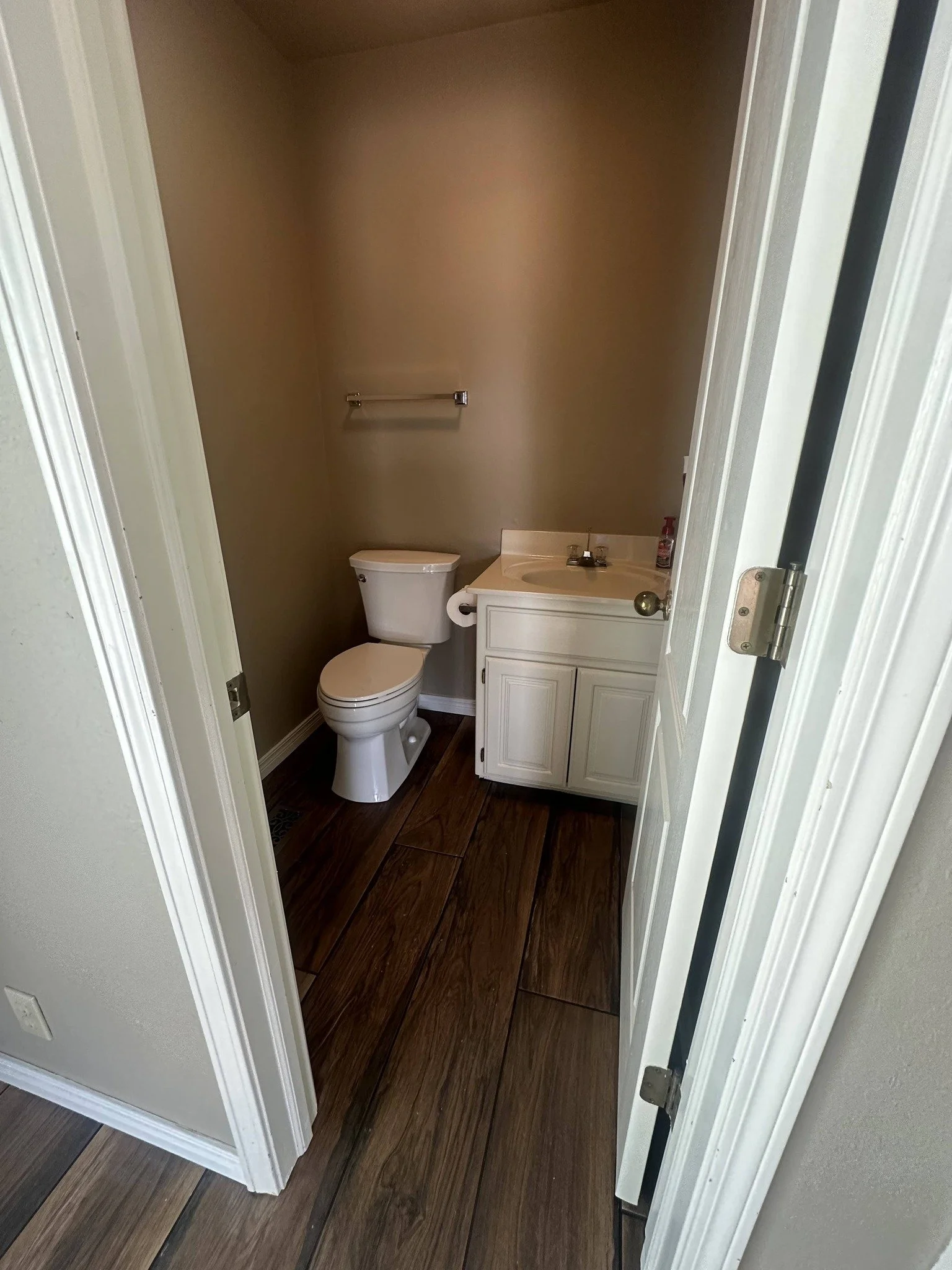 Small bathroom with a toilet, a small sink with cabinet, a towel bar, and dark wood flooring.