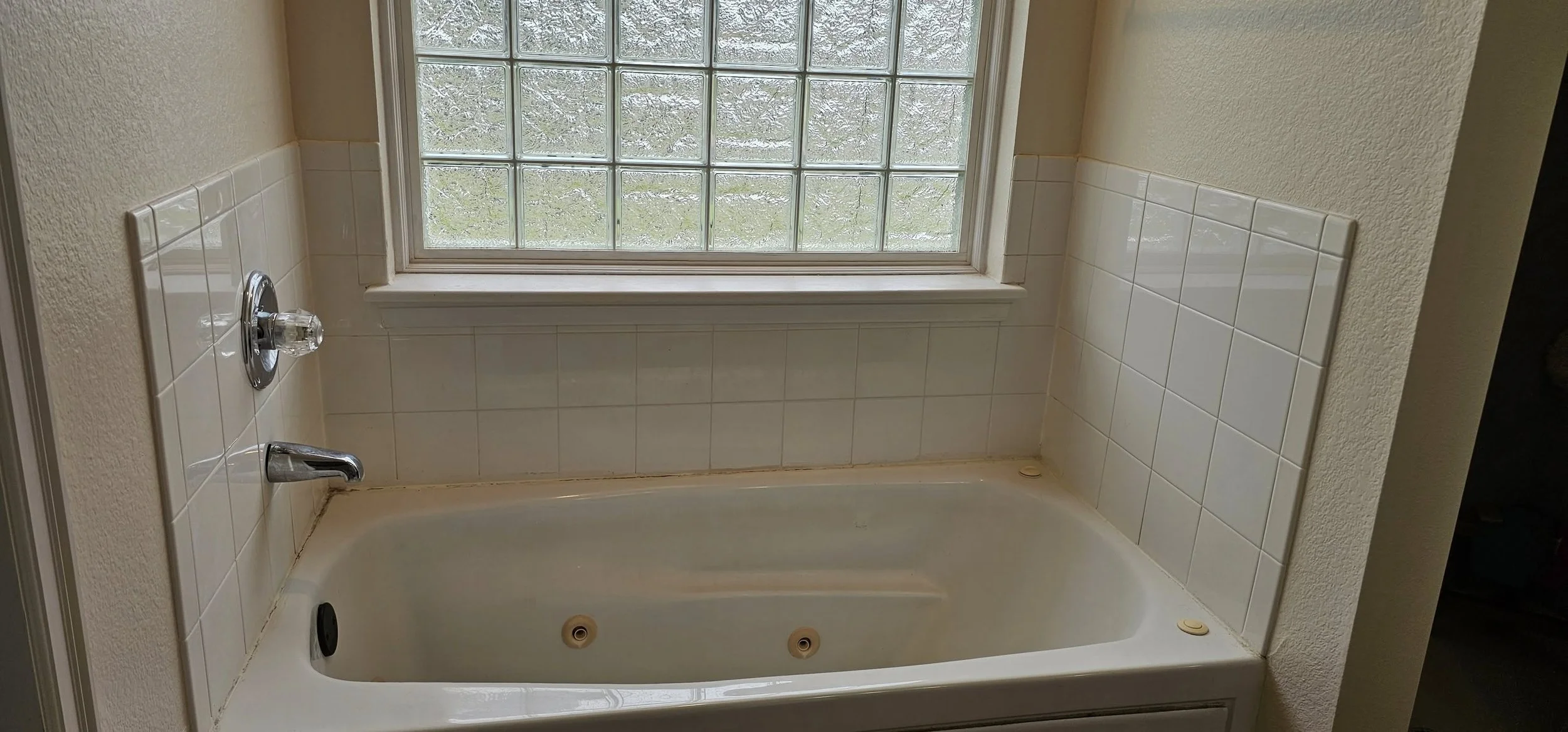 Bathroom with built-in bathtub, white tiles around the tub, and a window with glass blocks above the tub.