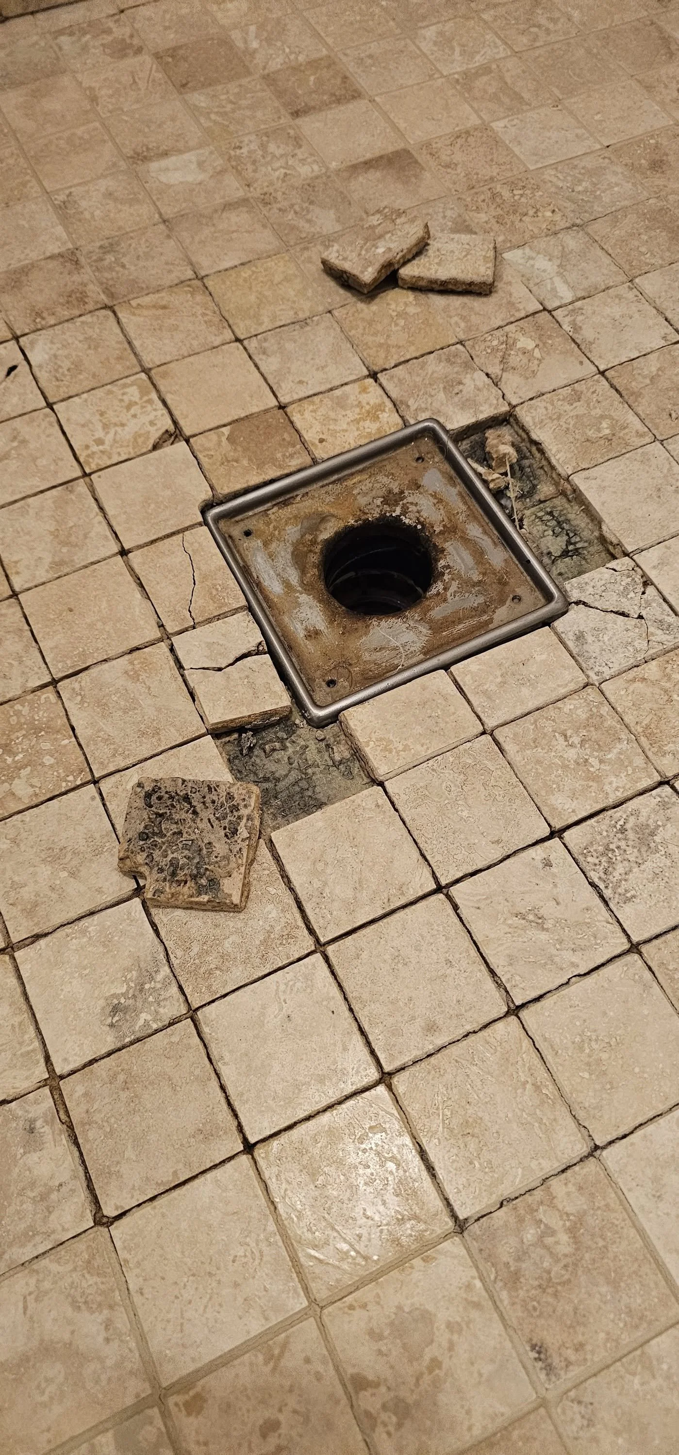 Broken floor tiles around a floor drain with some tiles and debris on the floor.