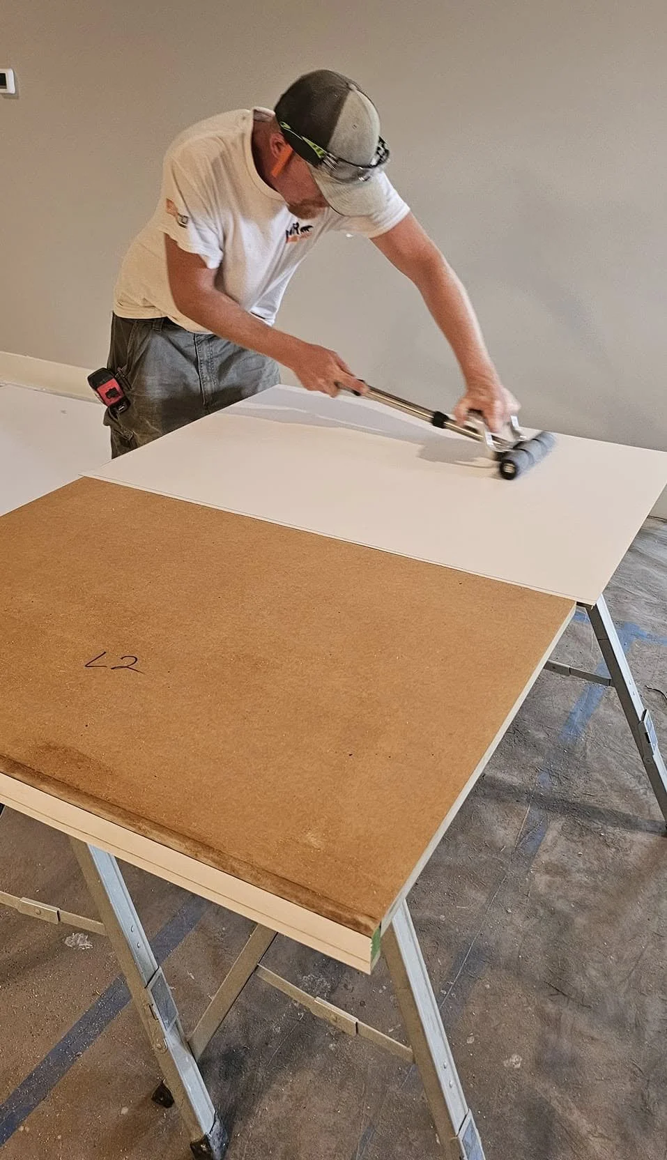 A person using a roller to apply a white wall covering or wallpaper to a large flat surface.