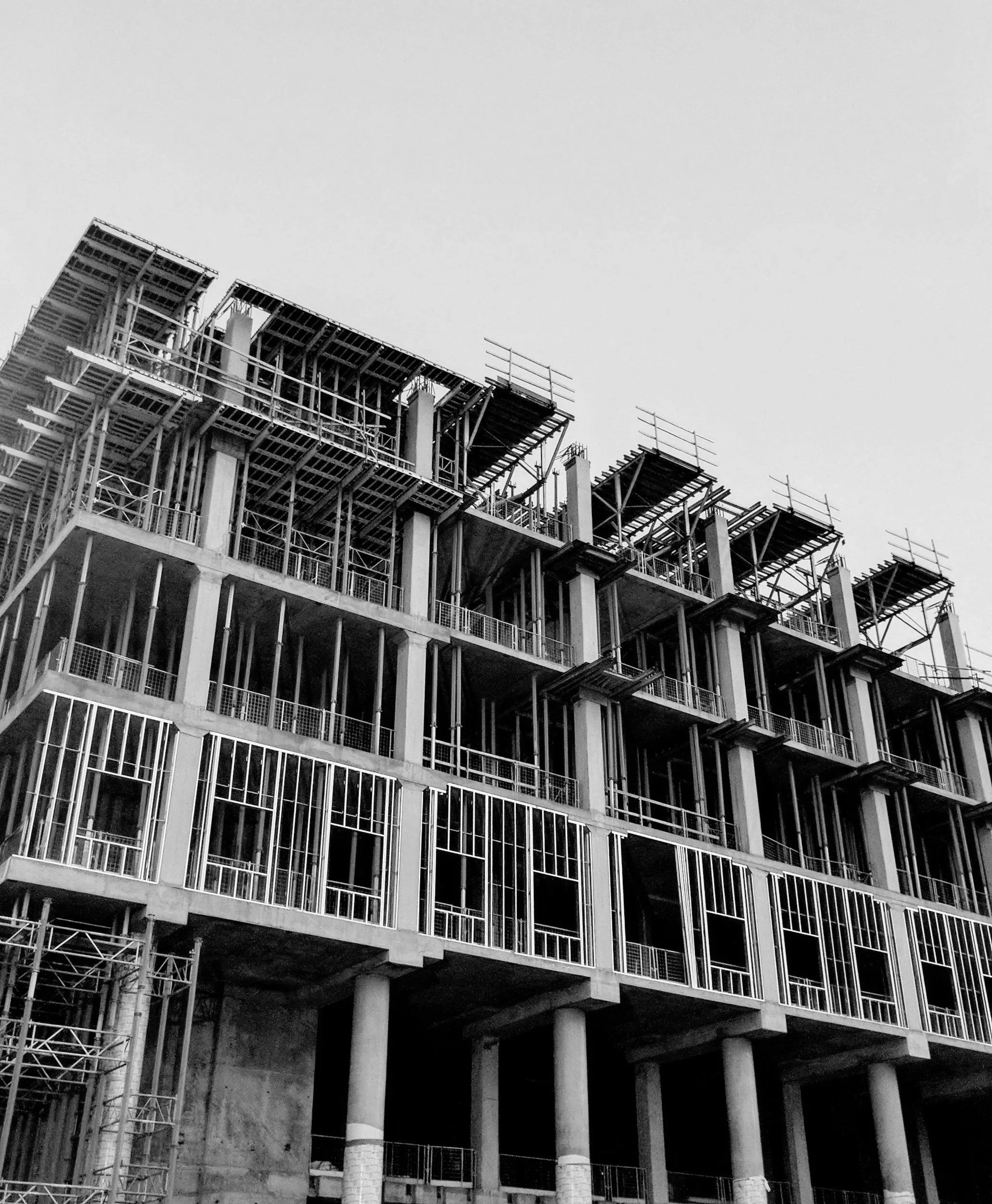 Black and white photo of a multi-story building under construction, showing scaffolding and exposed structural elements.