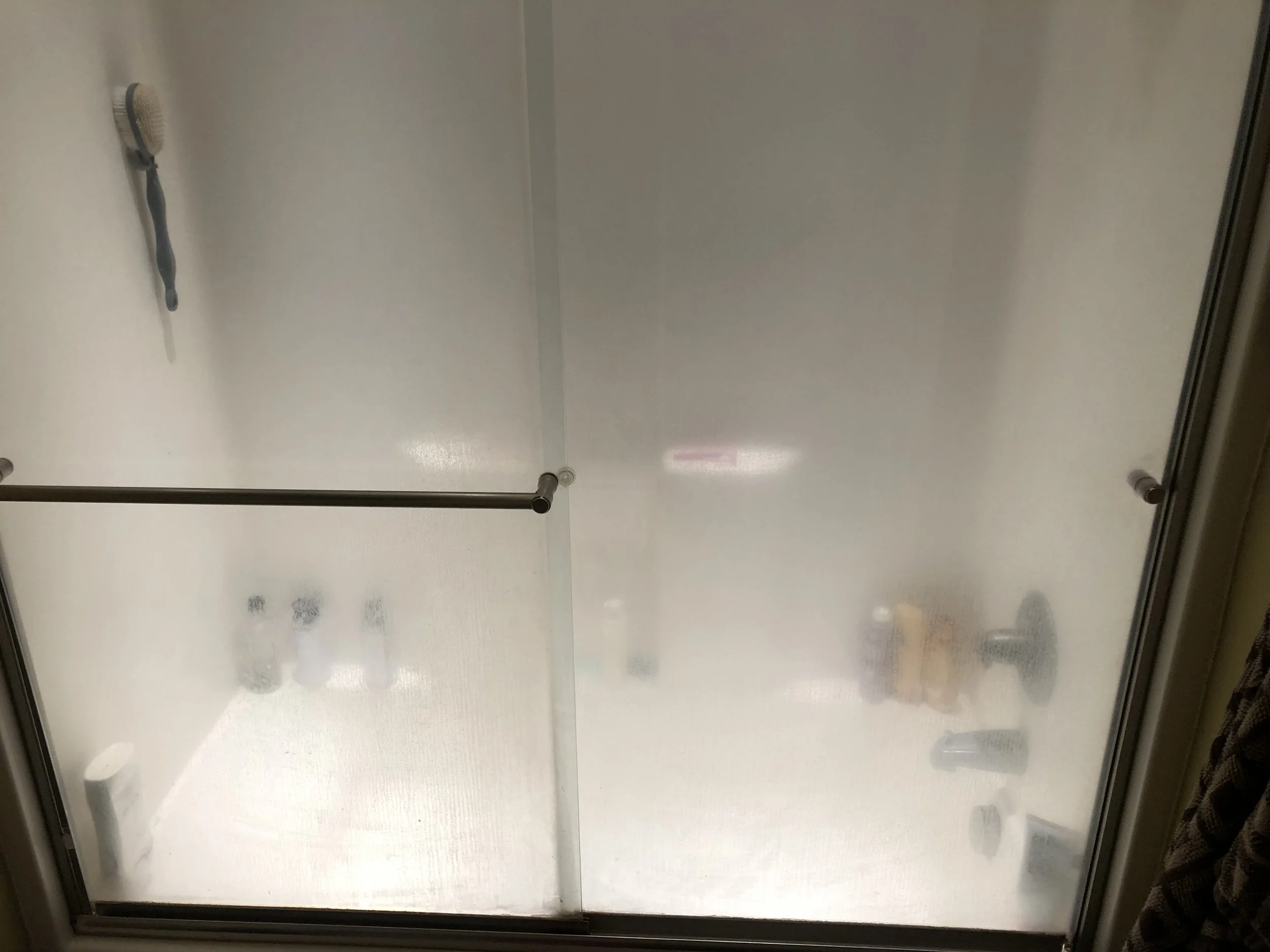 View of the inside of a shower with a handheld shower head attached to the wall and multiple small water spots on the glass door.
