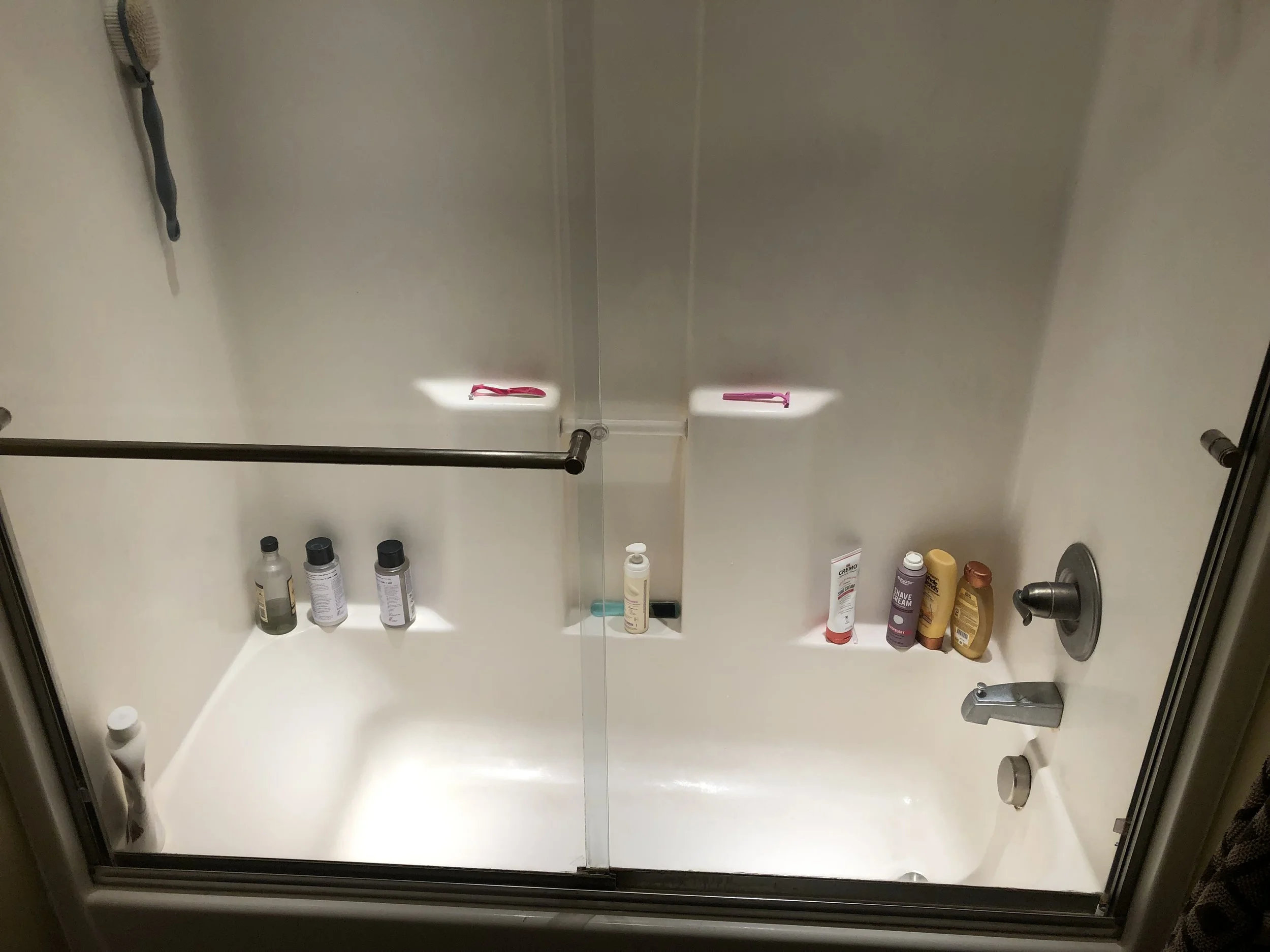 Bathroom medicine cabinet with various bottles of personal care products on the shelves, a toothbrush on the back wall, and a faucet and sink below.