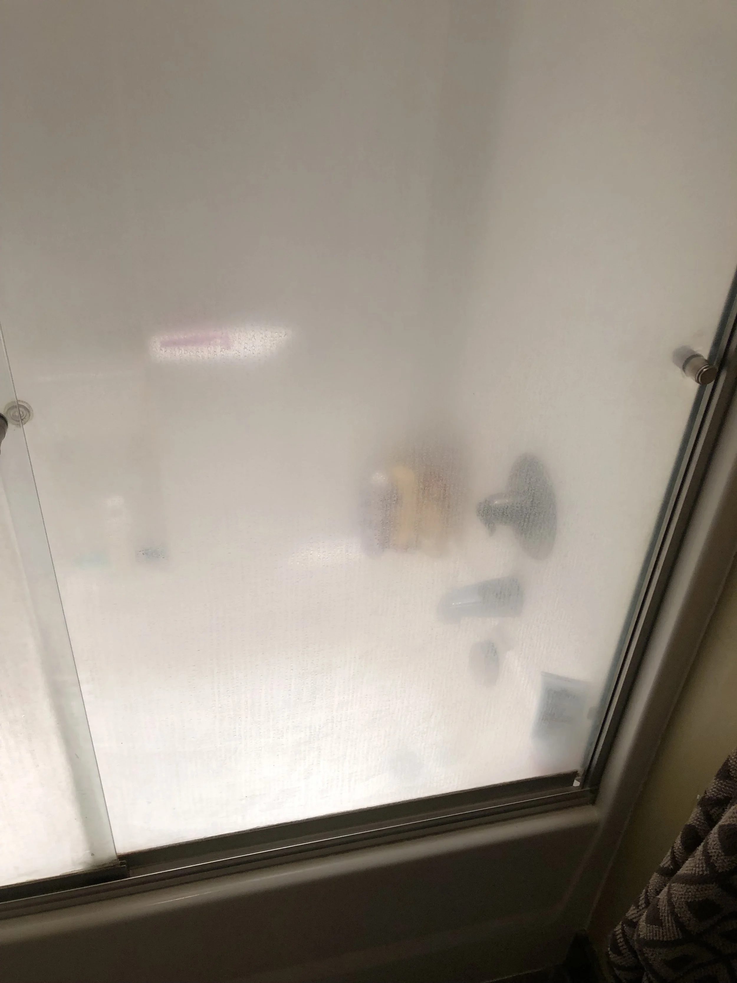View of a foggy window with frosted glass, through which a person's shadow and some objects are faintly visible outside.