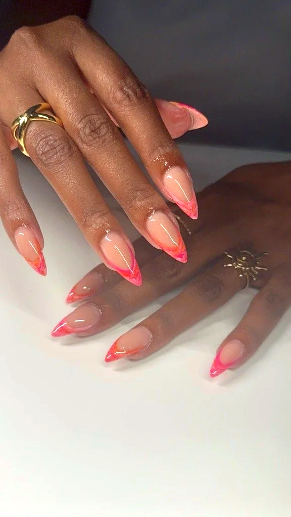 Close-up of a person's hand with freshly manicured nails featuring a pink and orange gradient design, adorned with gold rings.