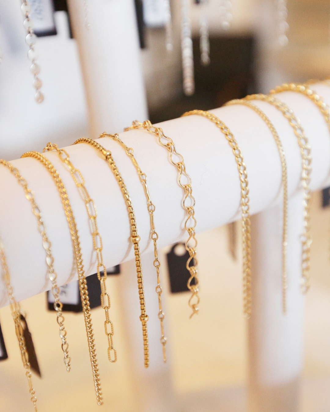 Various gold and silver chain bracelets displayed on a white jewelry stand.