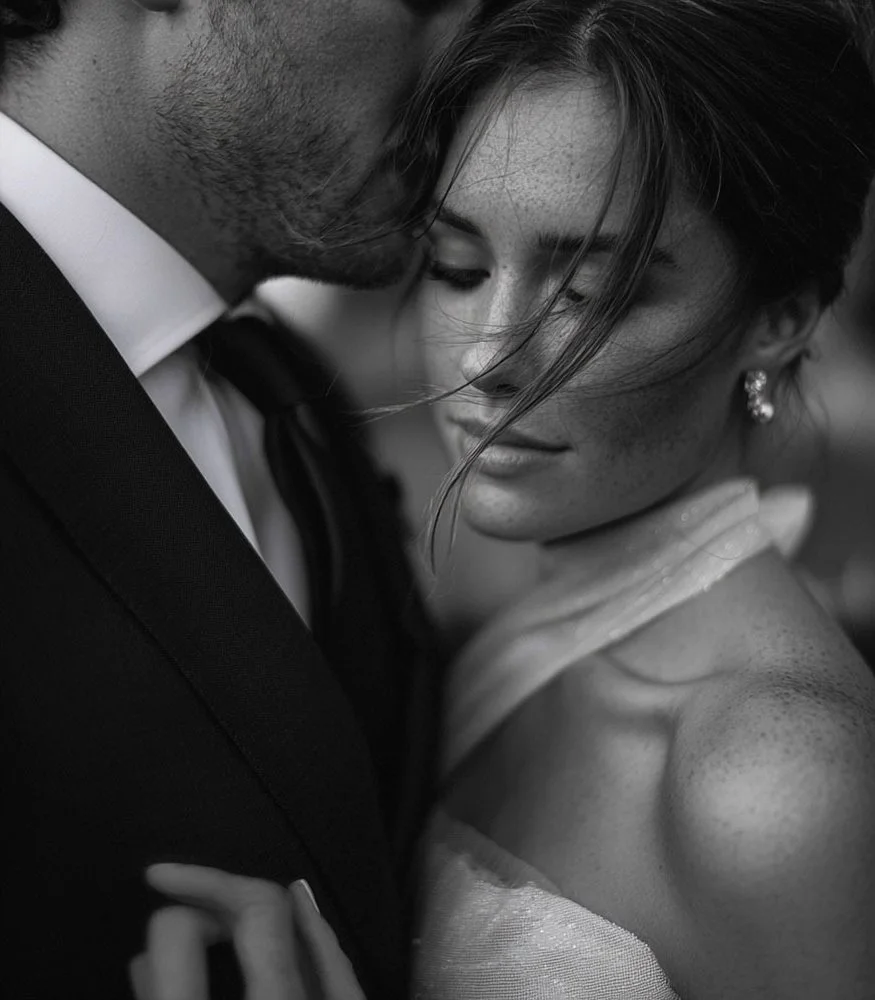 Close-up black and white photo of a couple embracing, with the woman's eyes closed, her face resting close to the man's face, showing intimacy.