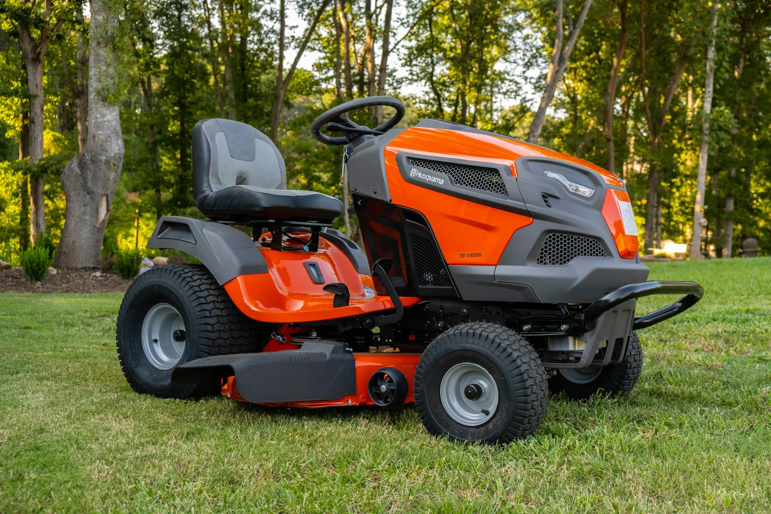 A bright orange and gray Husqvarna riding lawn mower on a lawn with trees in the background.