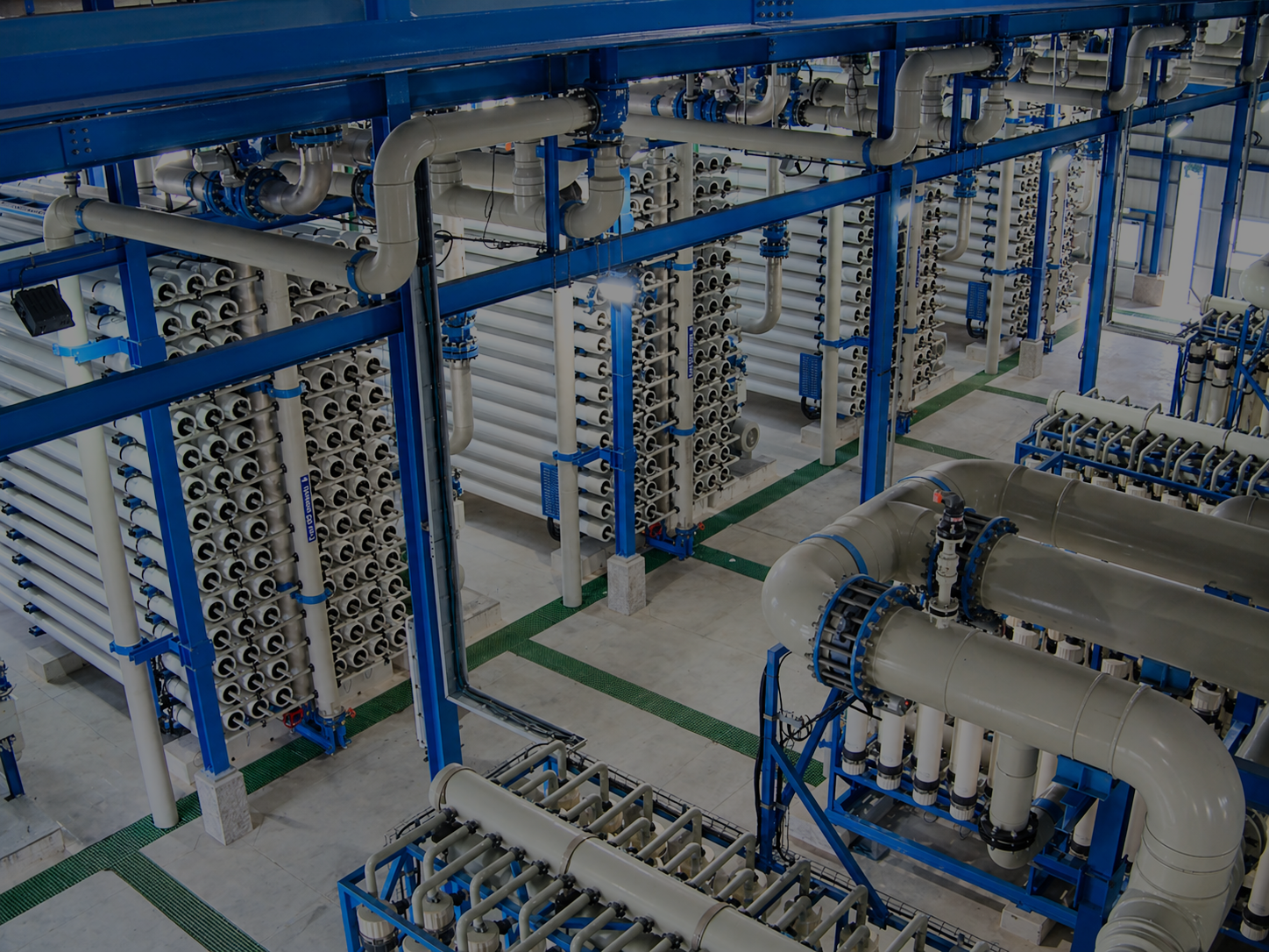 Desalination plant with large RO units, blue metal structures, and multiple filtration stages of reverse osmosis units connected by piping.