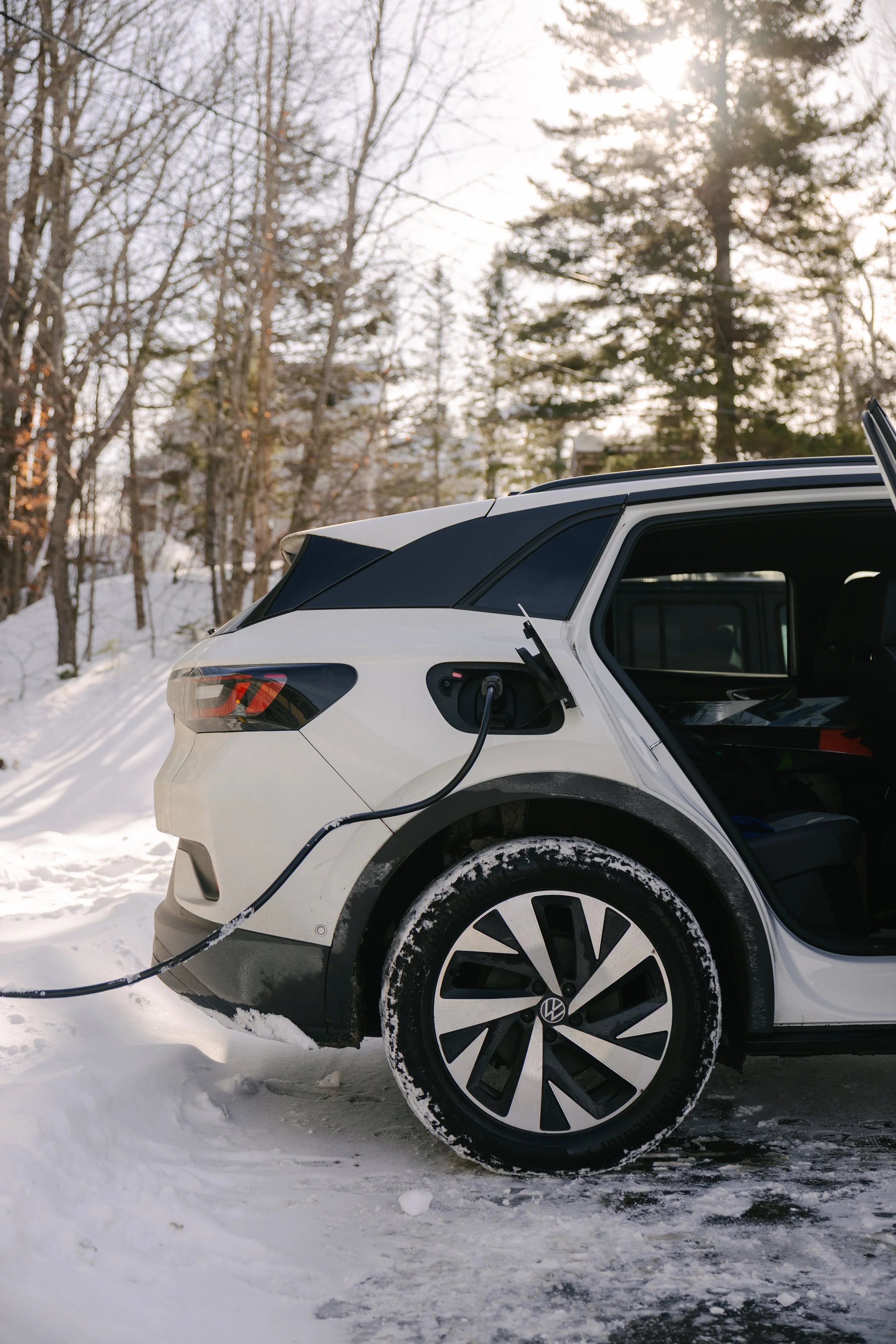 An electric vehicle charging in a snowy outdoor setting with trees in the background.