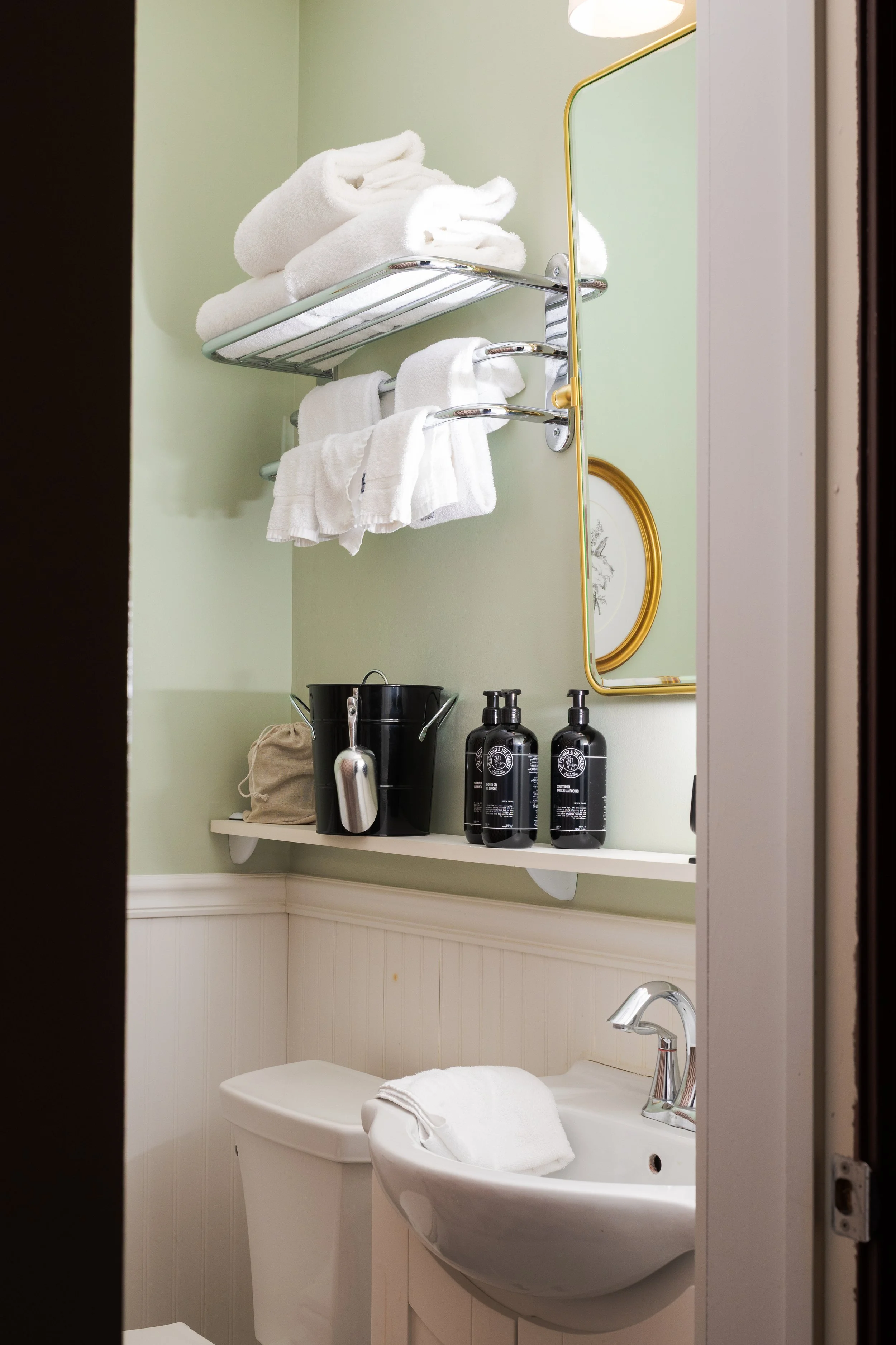 A close-up of a small bathroom corner with towels on a shelf, toiletries, a mirror, and a sink.