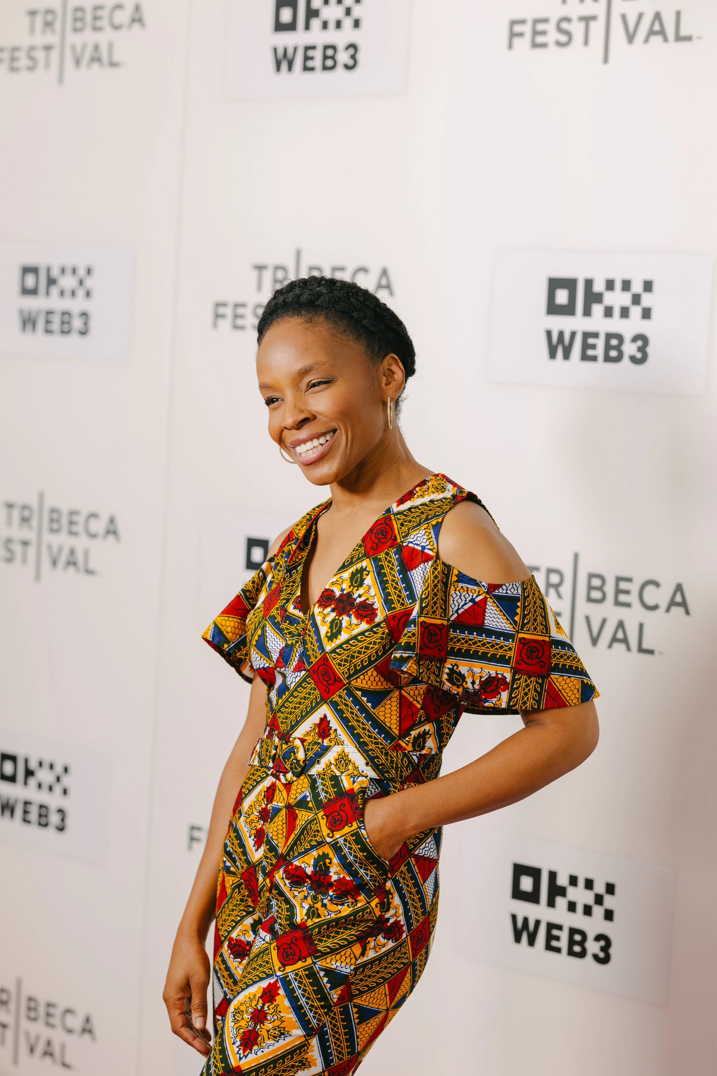 Smiling woman with short, curly hair wearing a colorful patterned jumpsuit at Tribeca Film Festival