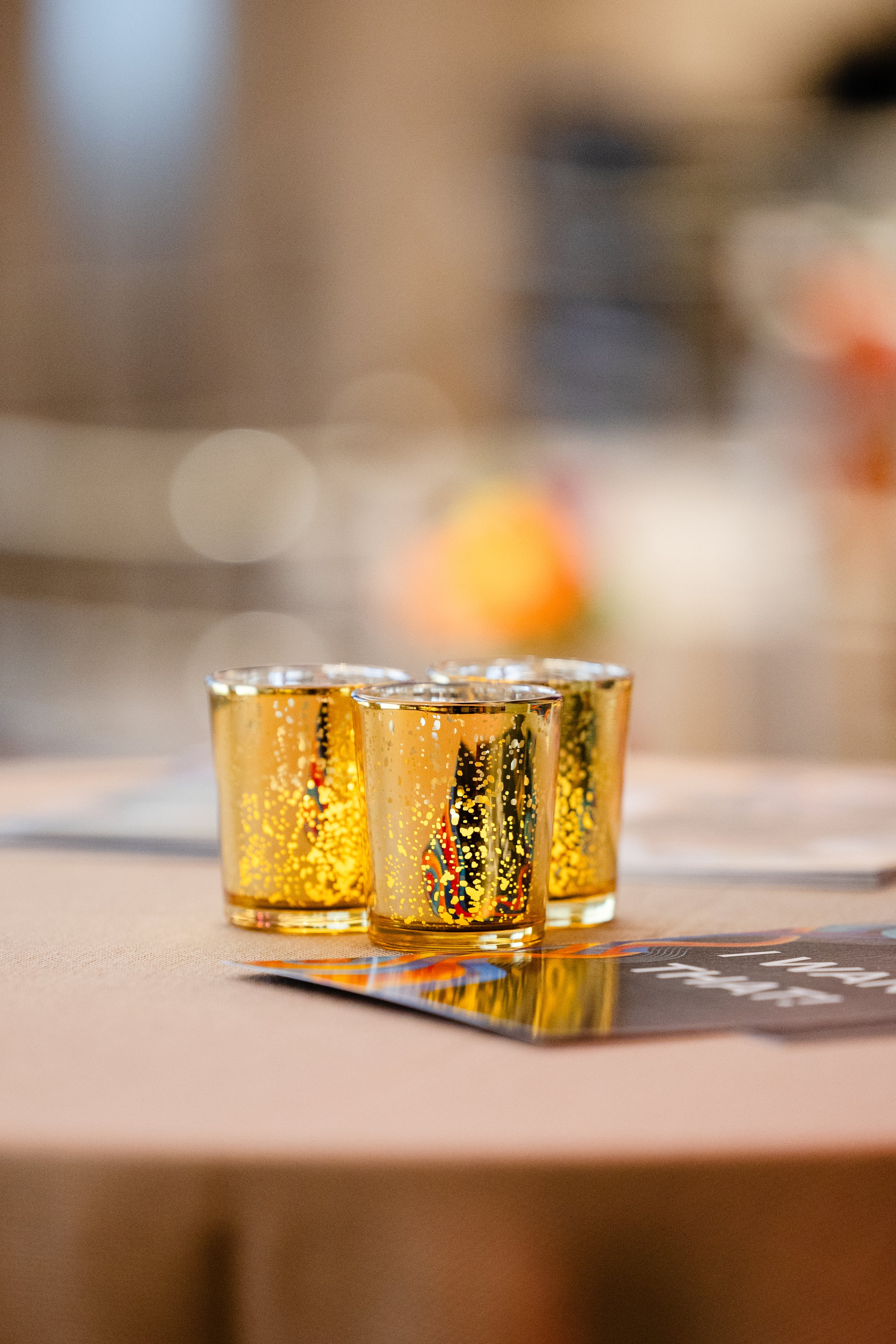 Three small transparent glasses filled with a golden beverage, placed on a table with a blurred background.