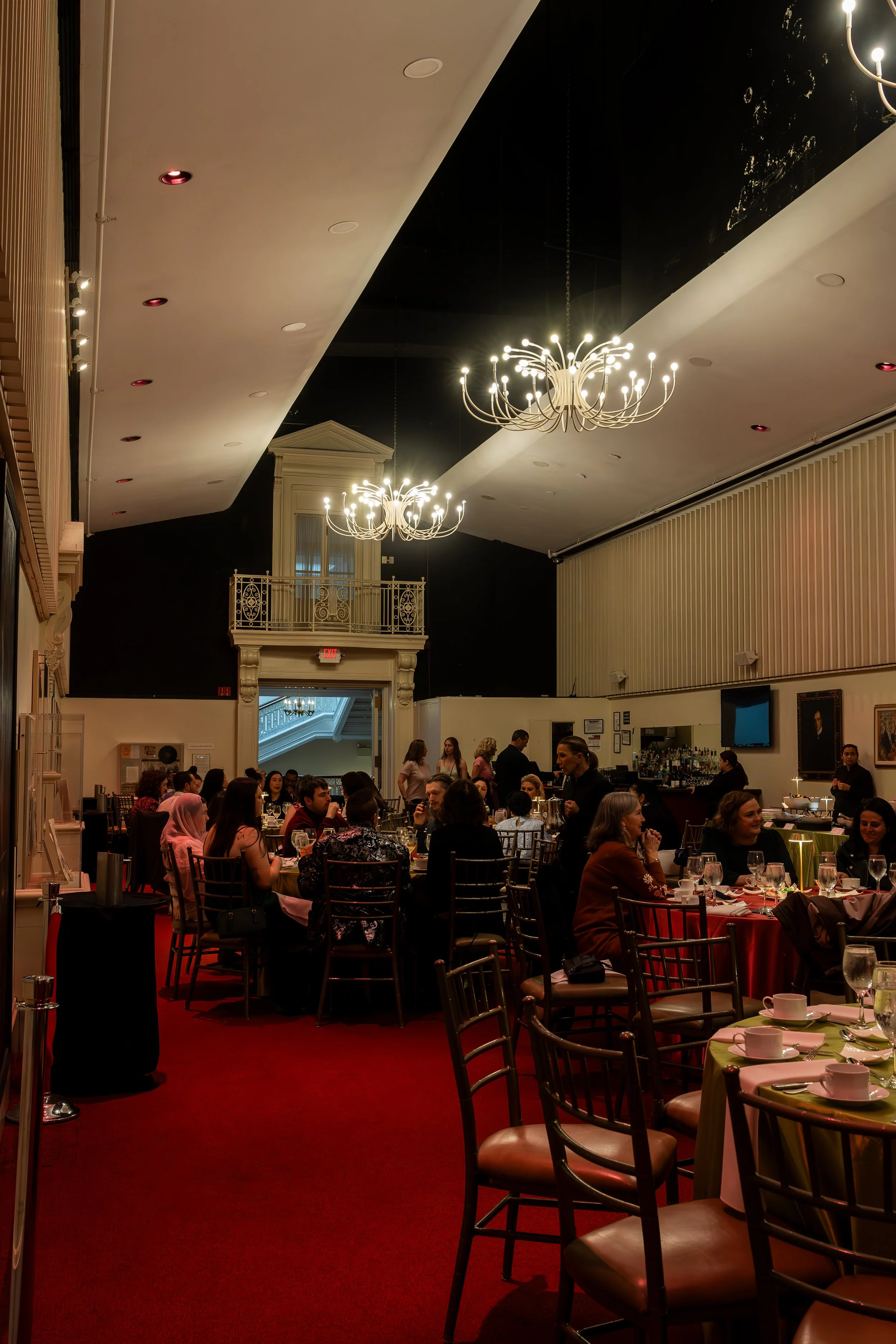 Elegant restaurant dining area with chandeliers, black and white walls, and patrons seated at tables with colorful tablecloths.